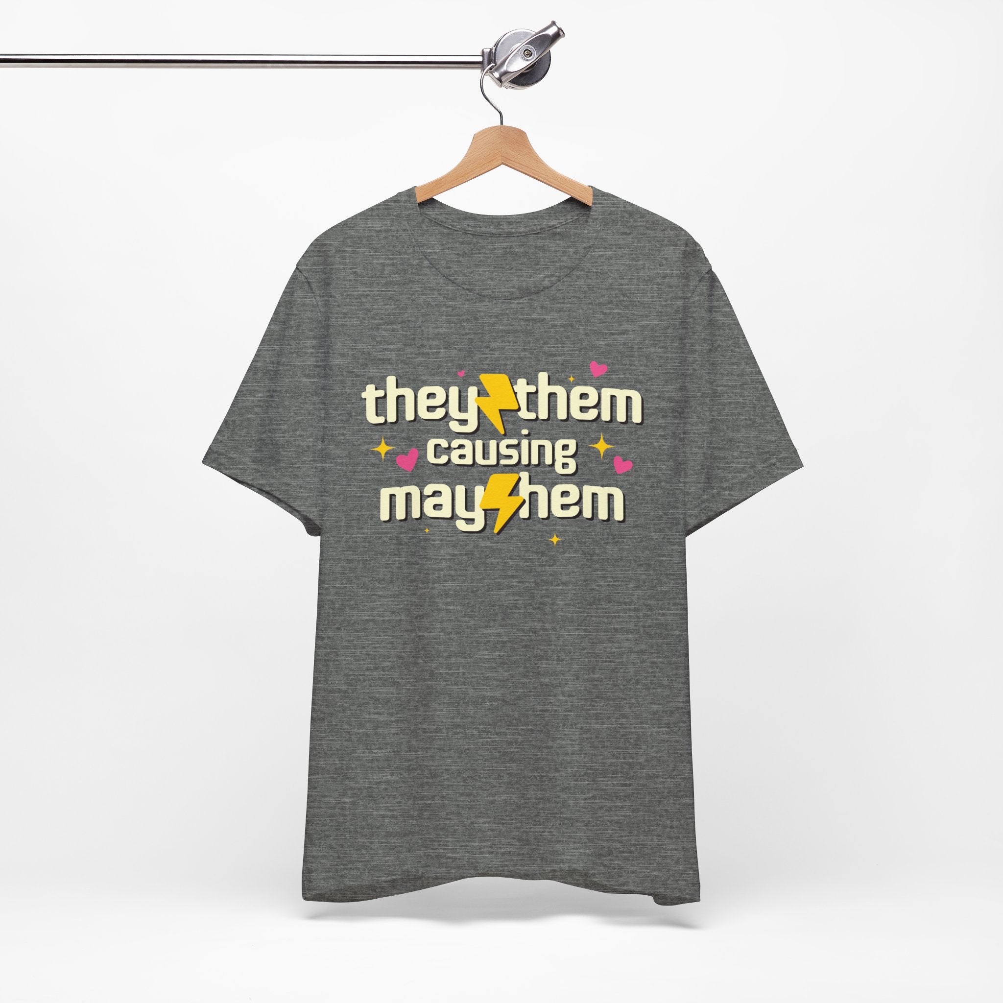 Gray t-shirt with 'they/them causing mayhem' text on a hanger against a white background