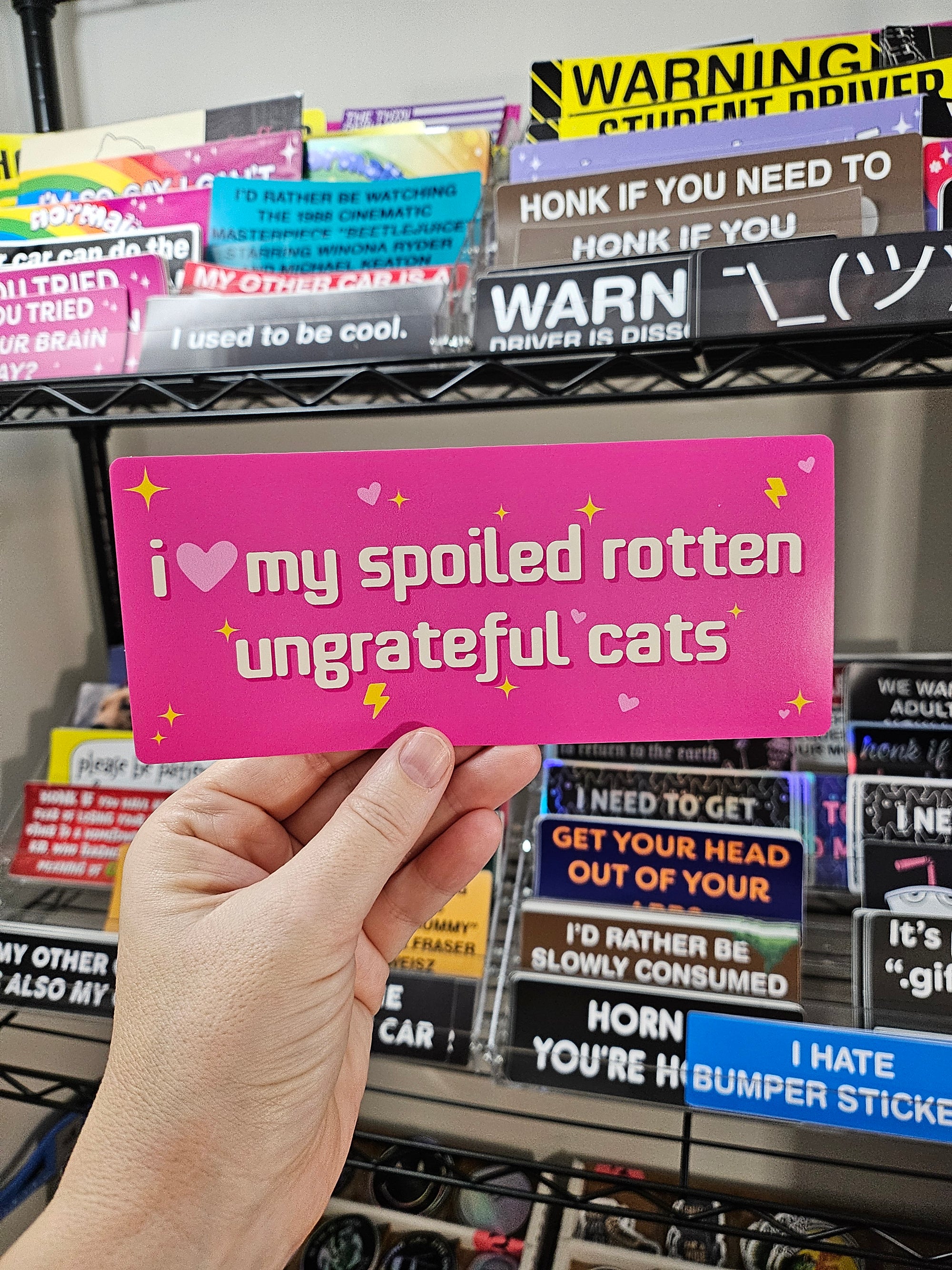 rectangular bumper stickers that say “I love my spoiled rotten ungrateful cats,” shown in pink with hearts, sparkles, and lightning bolts.
