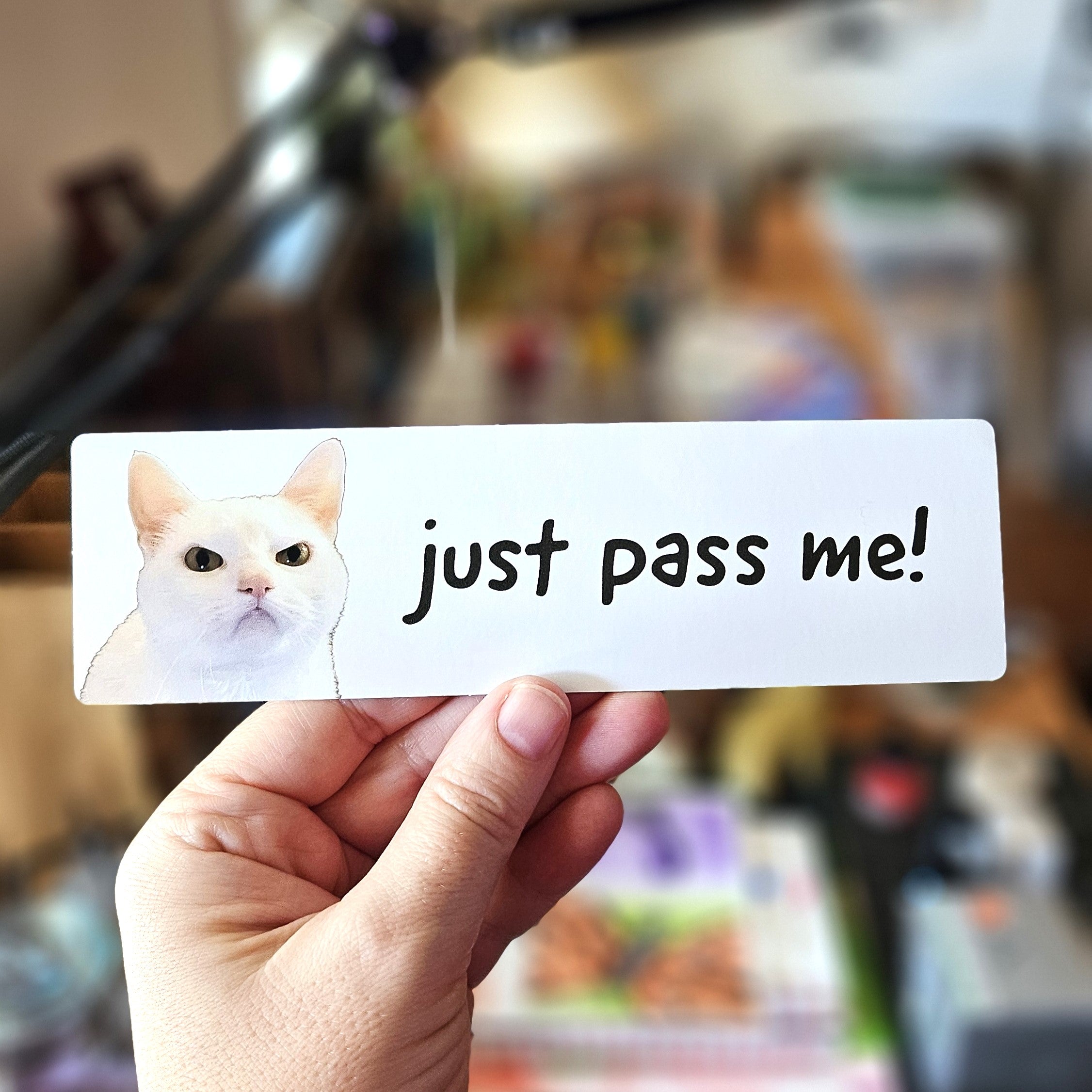 A white bumper stickers with the text 'just pass me!' and an image of a white mad cat