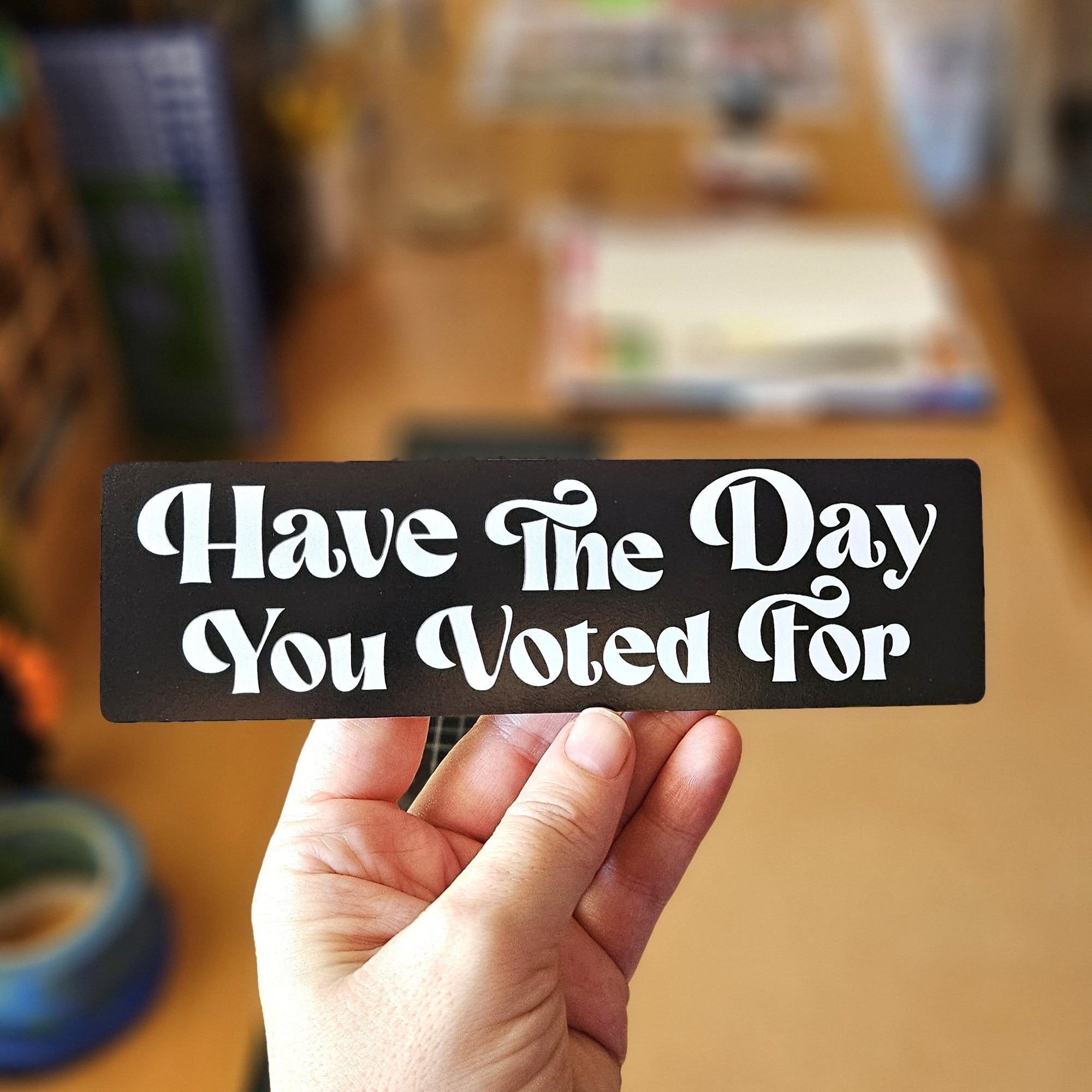 rectangular vinyl sticker that say “Have the Day You Voted For,” shown with white text on black backgrounds.
