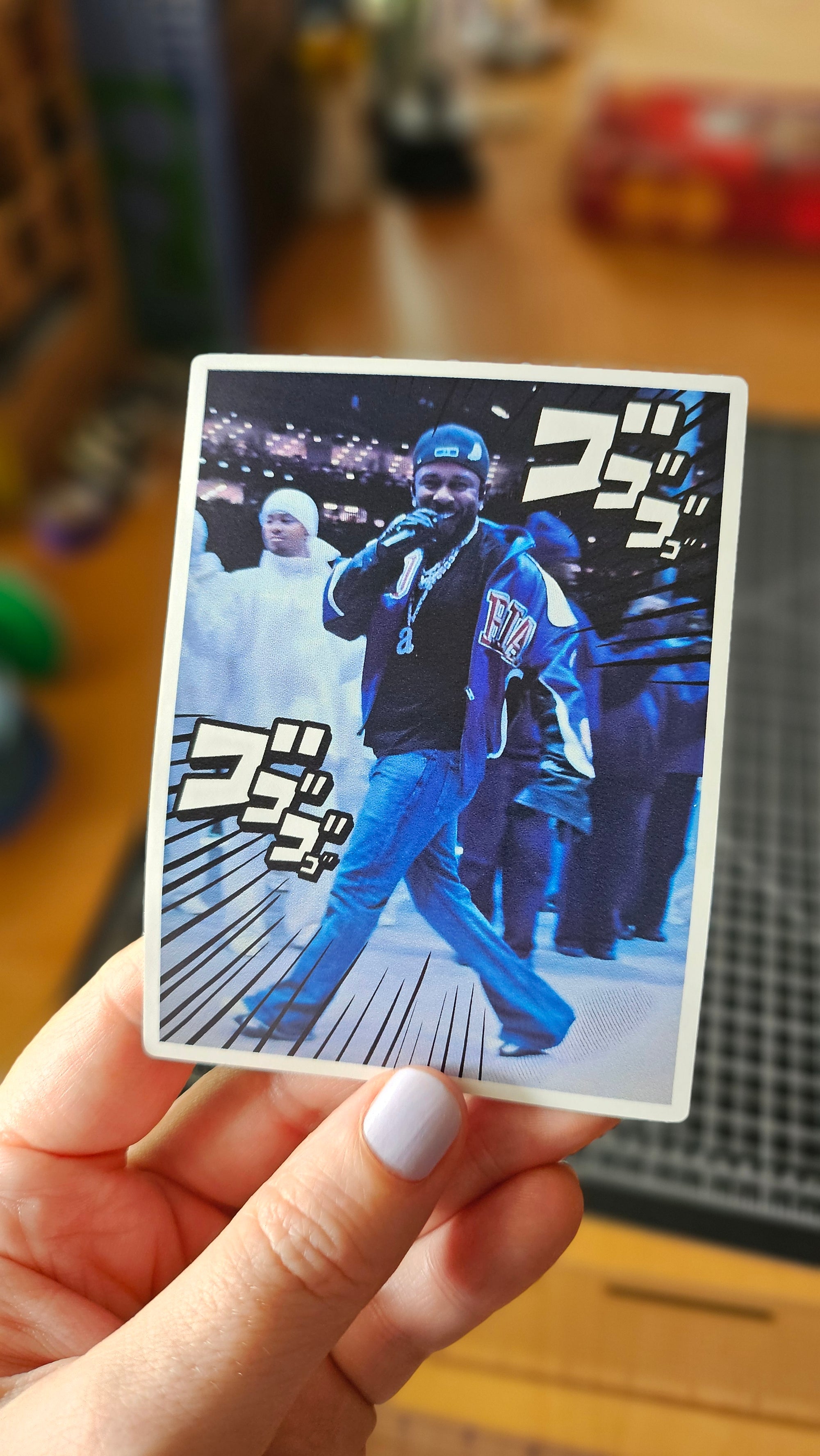 Rectangular photo-style sticker featuring a rapper walking through a blue-toned scene with bold manga-style action text accents.
