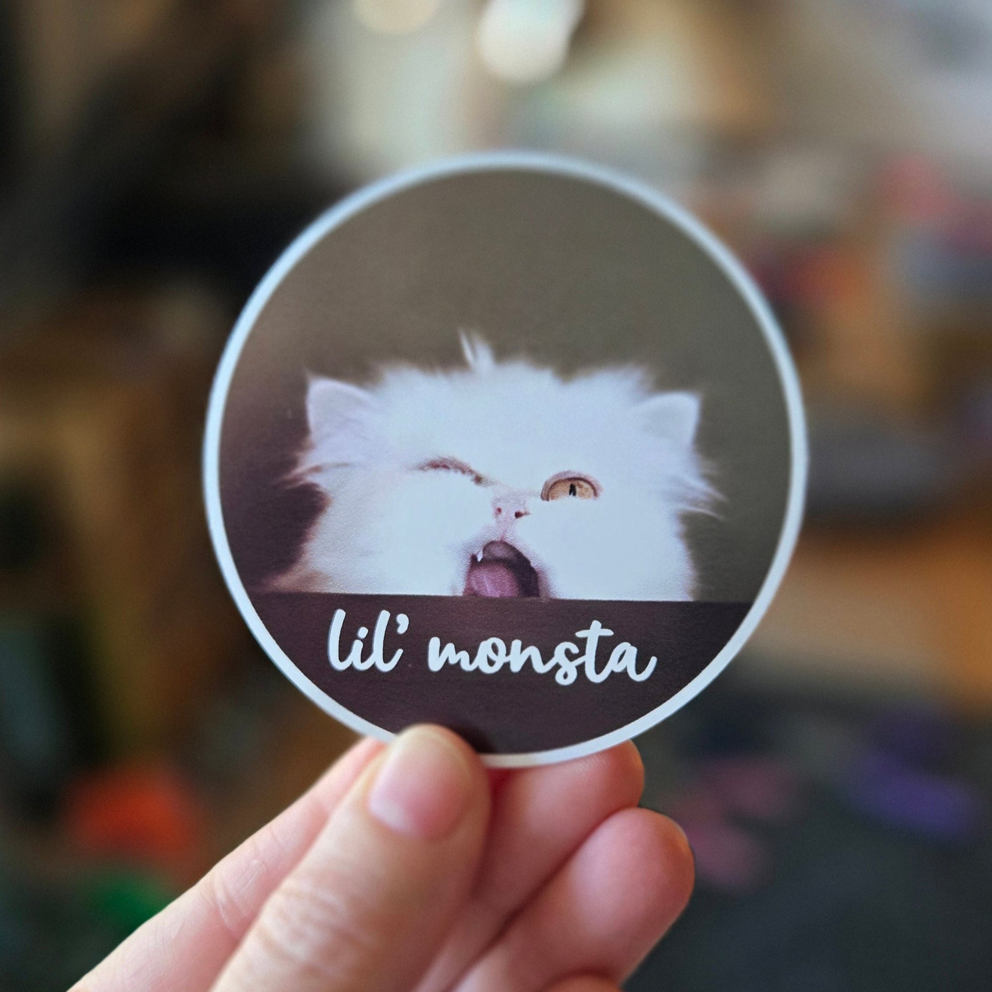 Circular sticker with a fluffy white cat and 'lil' monsta' text on a brown background
