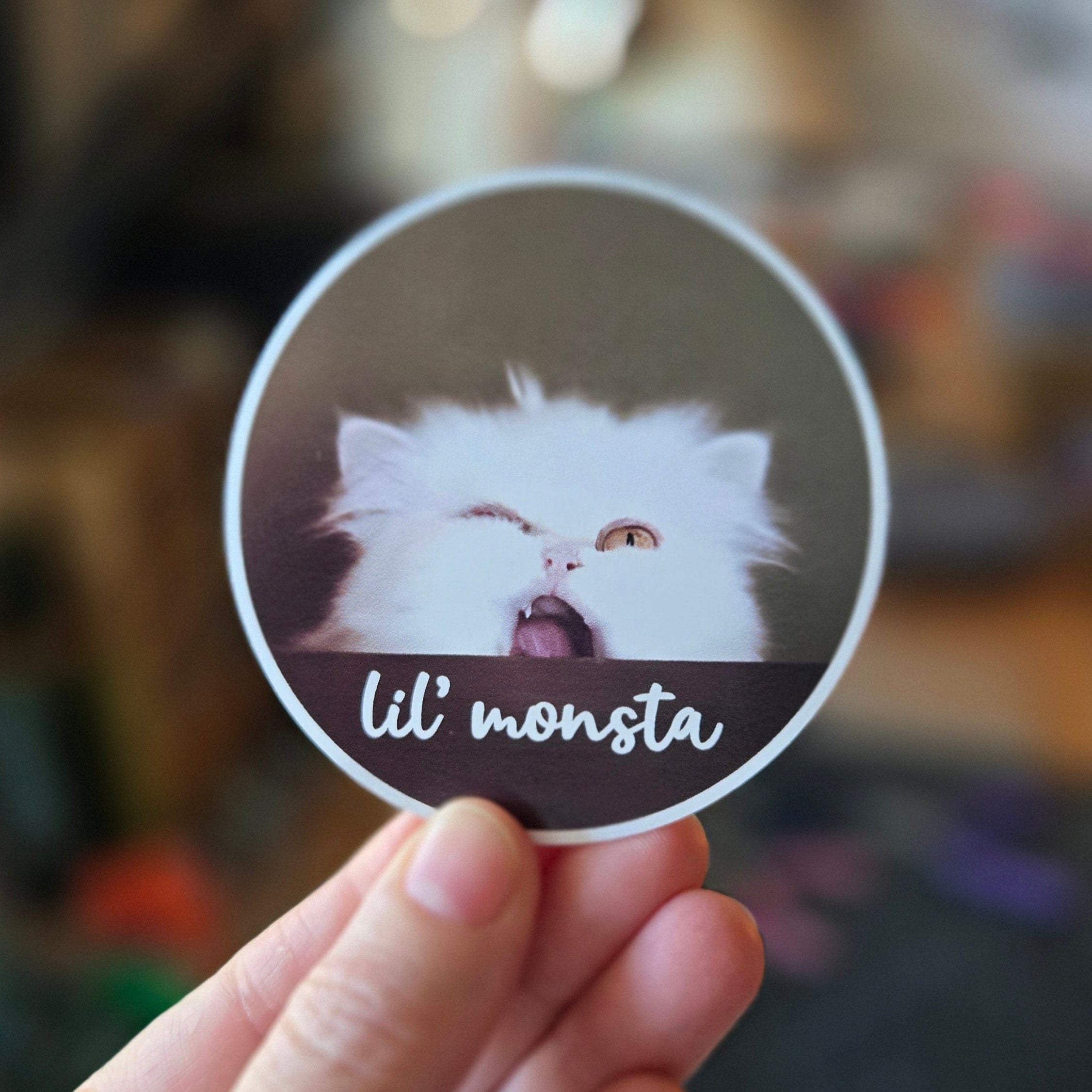Circular sticker with a fluffy white cat and 'lil' monsta' text on a brown background