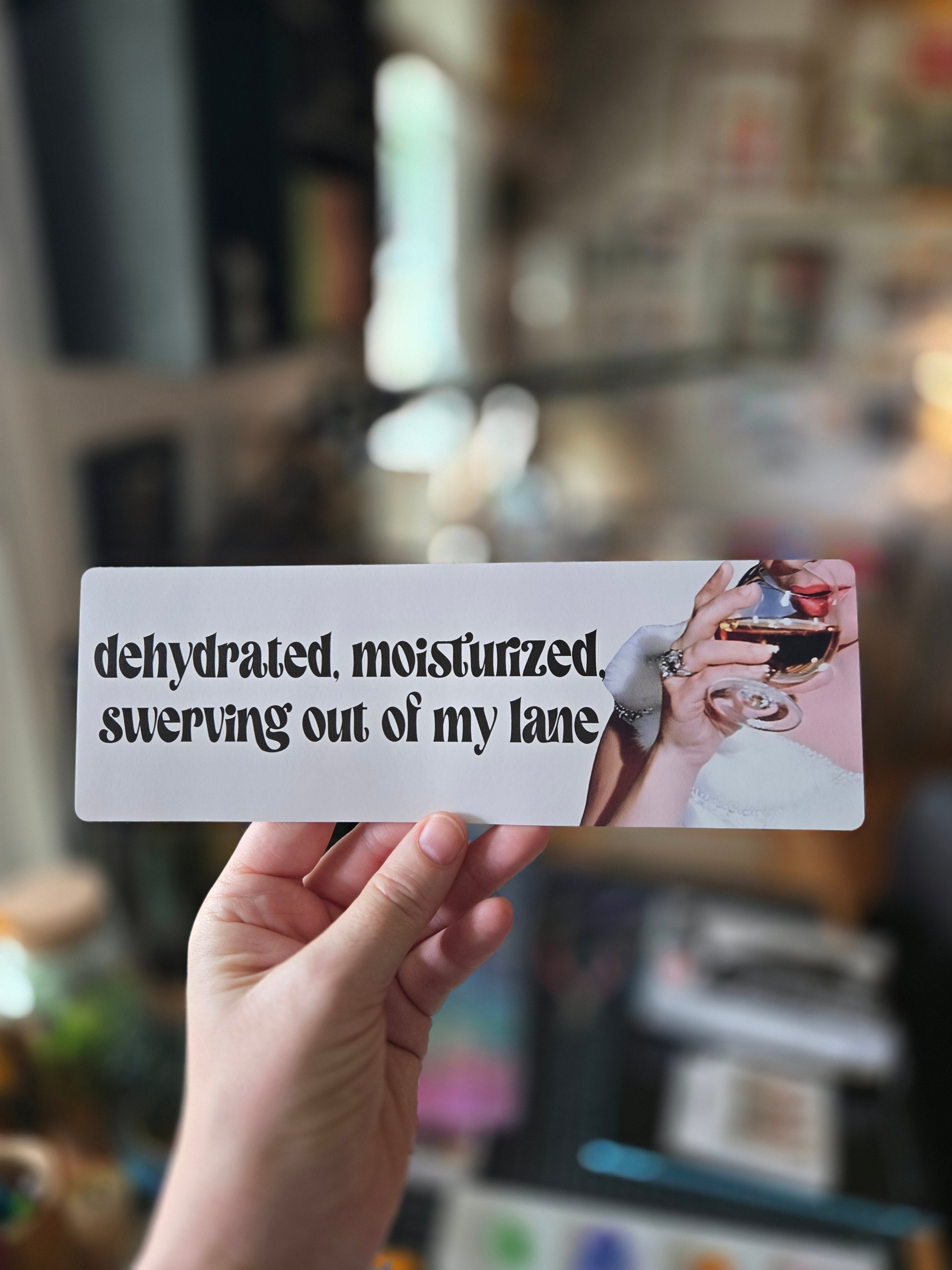 A vinyl sticker with the phrase 'dehydrated, moisturized, swerving out of my lane' printed on it, alongside an image of a person holding a drink.