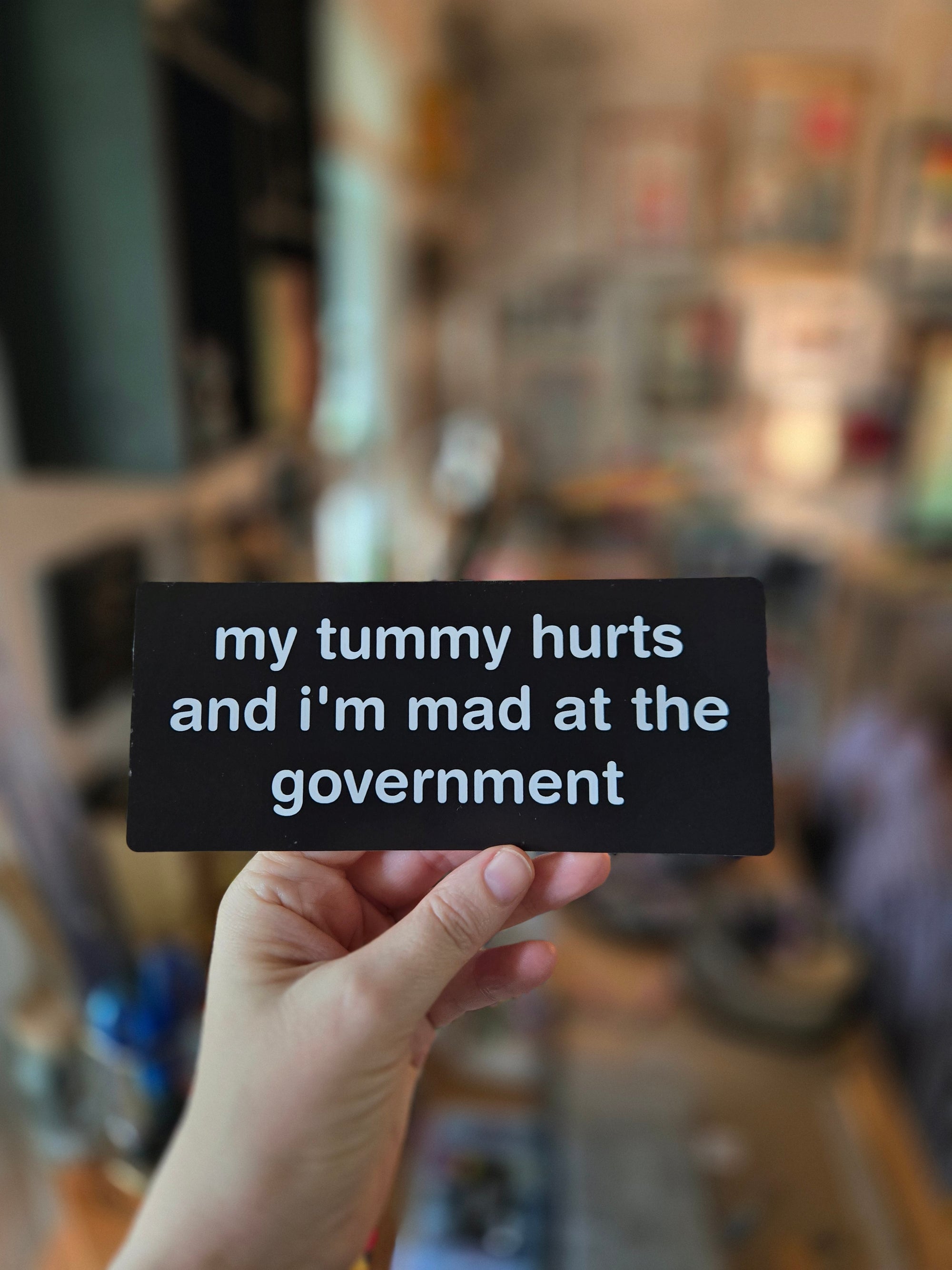 Hand holding a black card with text in a blurred indoor setting