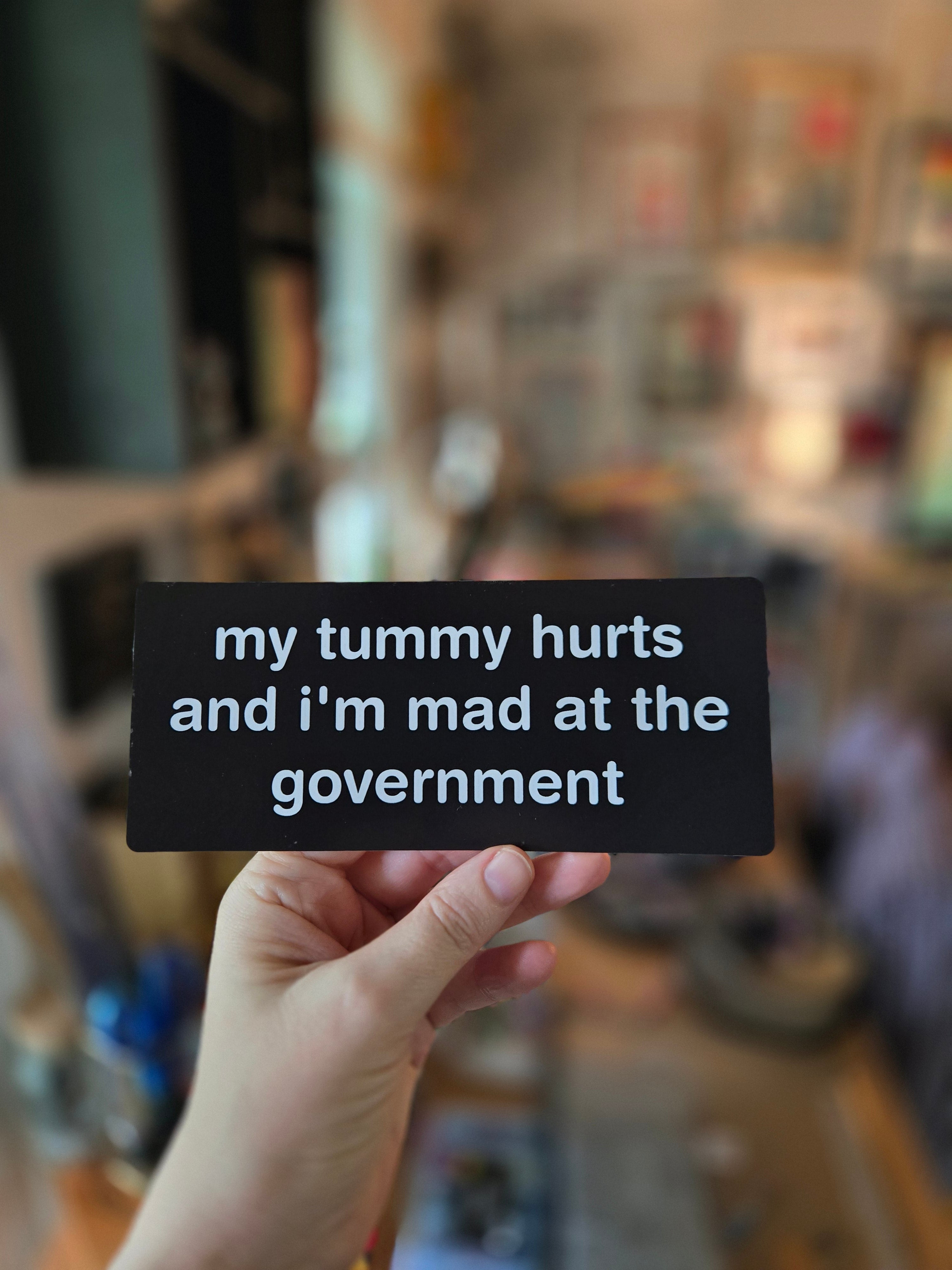 Hand holding a black card with text in a blurred indoor setting