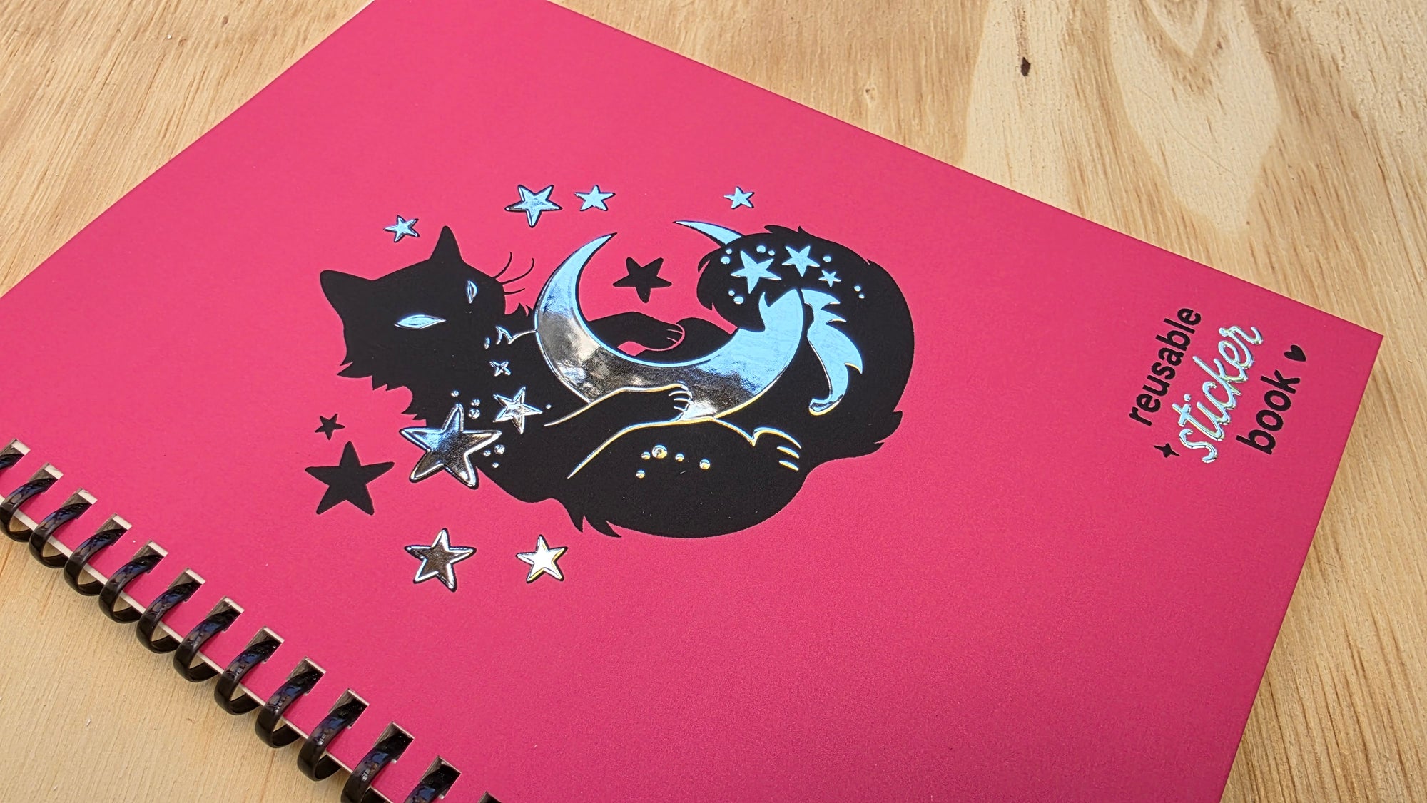 Pink stickerbook with black cat and unicorn design on a wooden surface