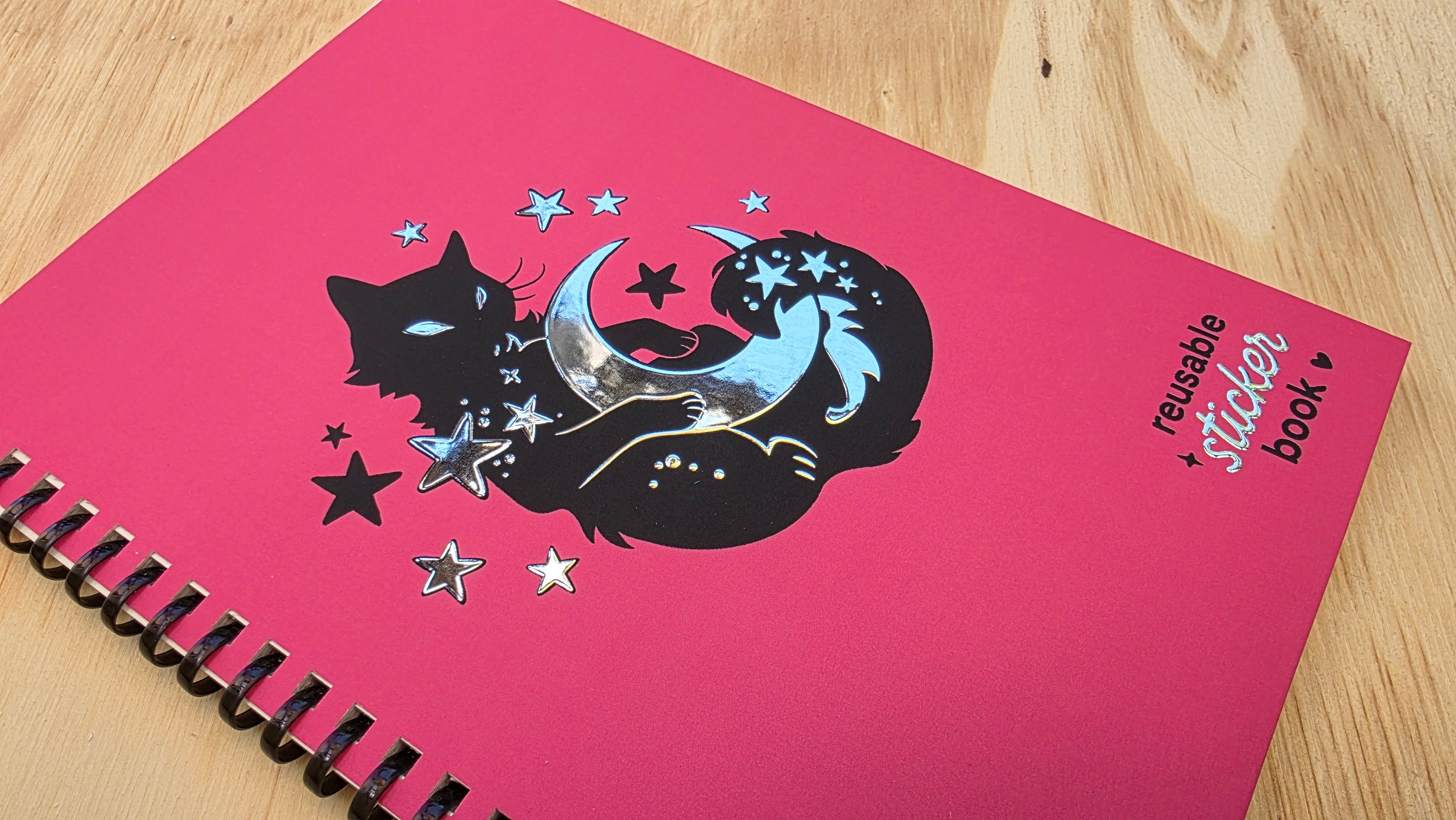 Pink stickerbook with black cat and unicorn design on a wooden surface