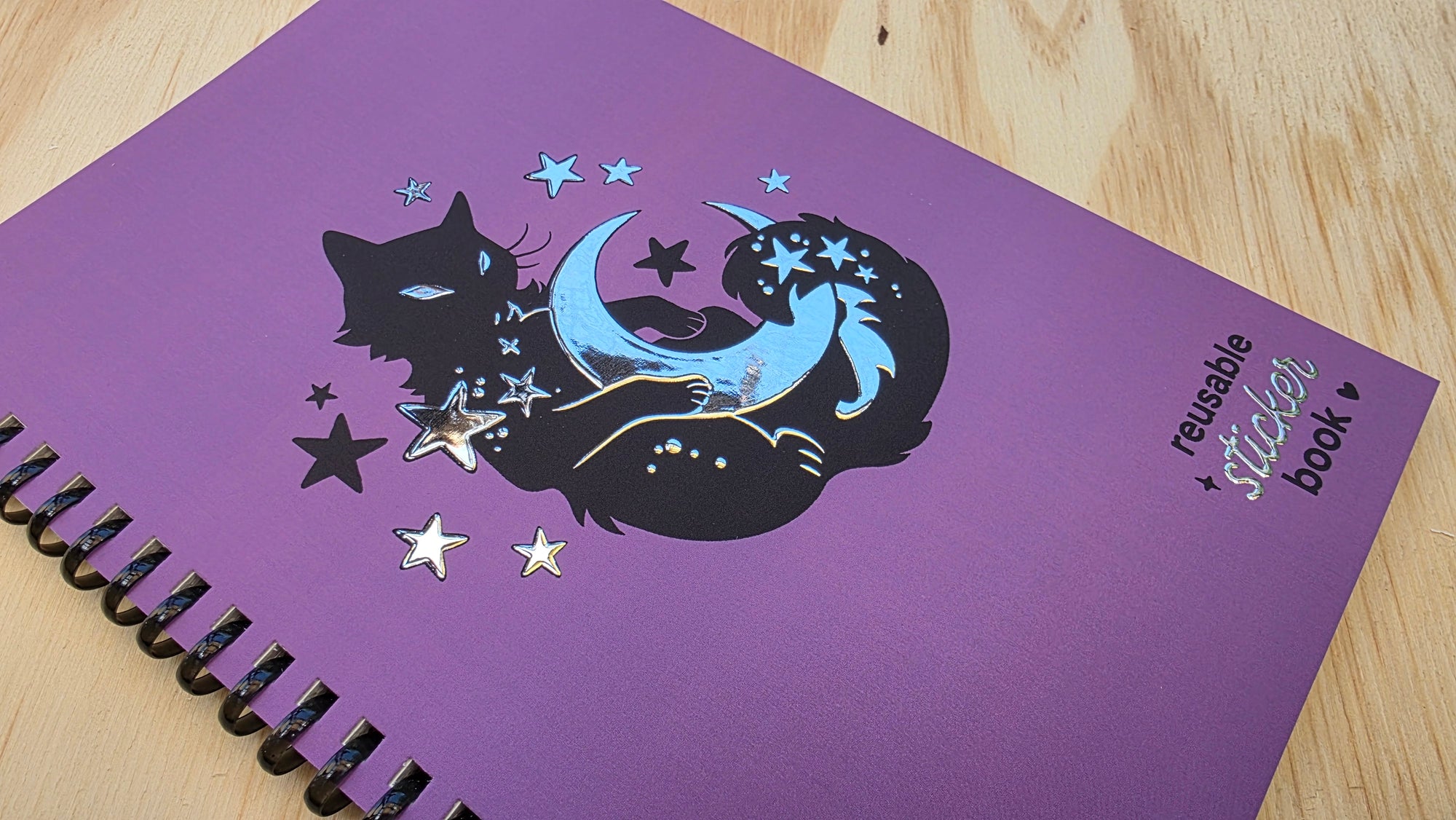 Purple notebook with black cat and unicorn design on a wooden surface