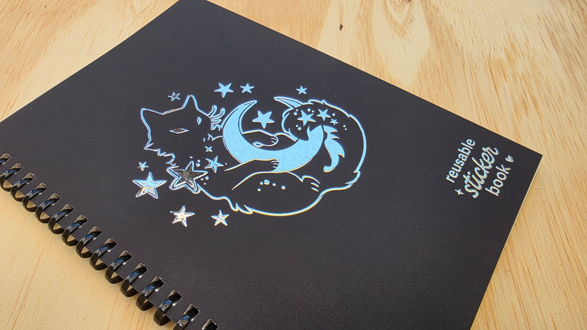 Black notebook with cat and moon design on a wooden surface