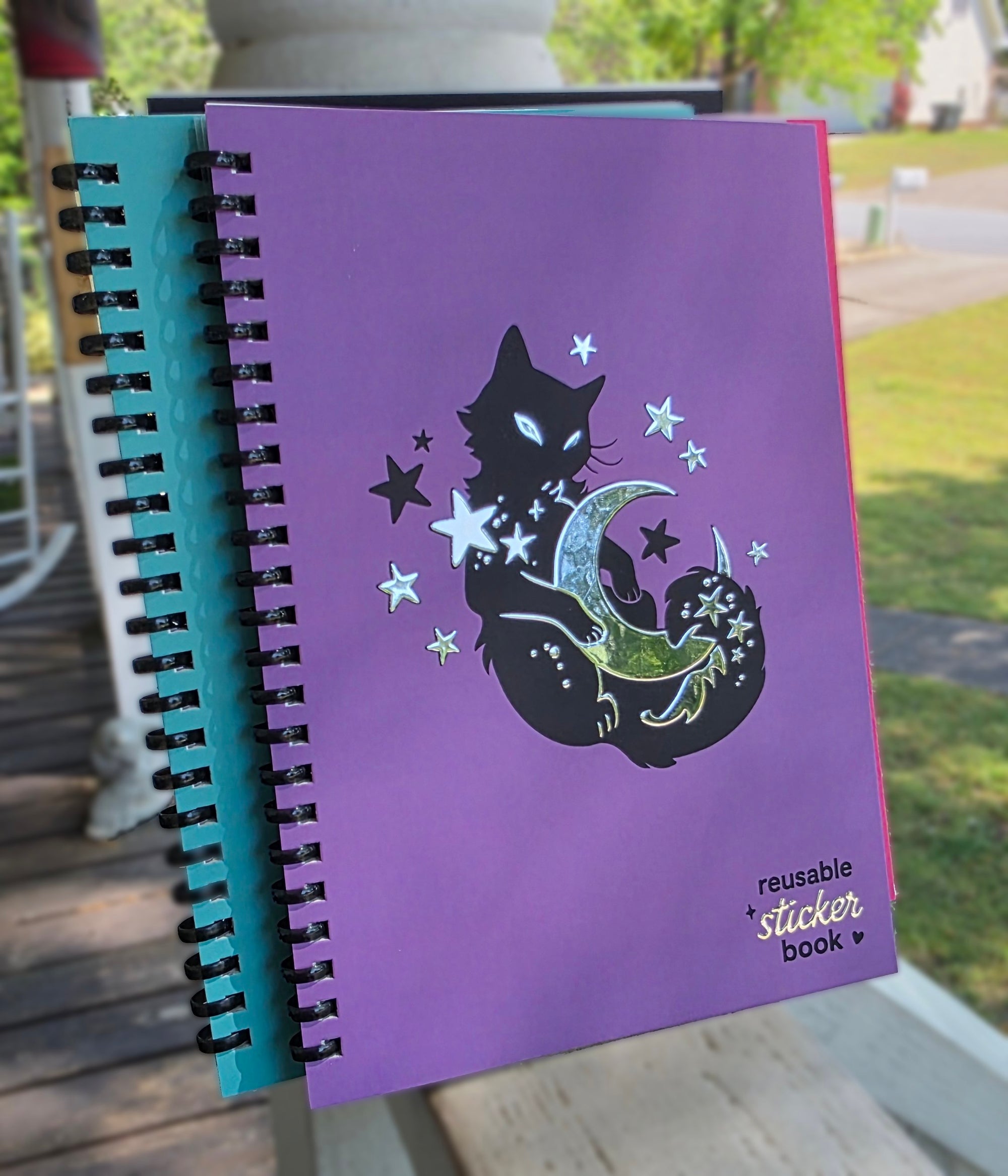 Purple reusable sticker book with a cat and moon design on a wooden surface.