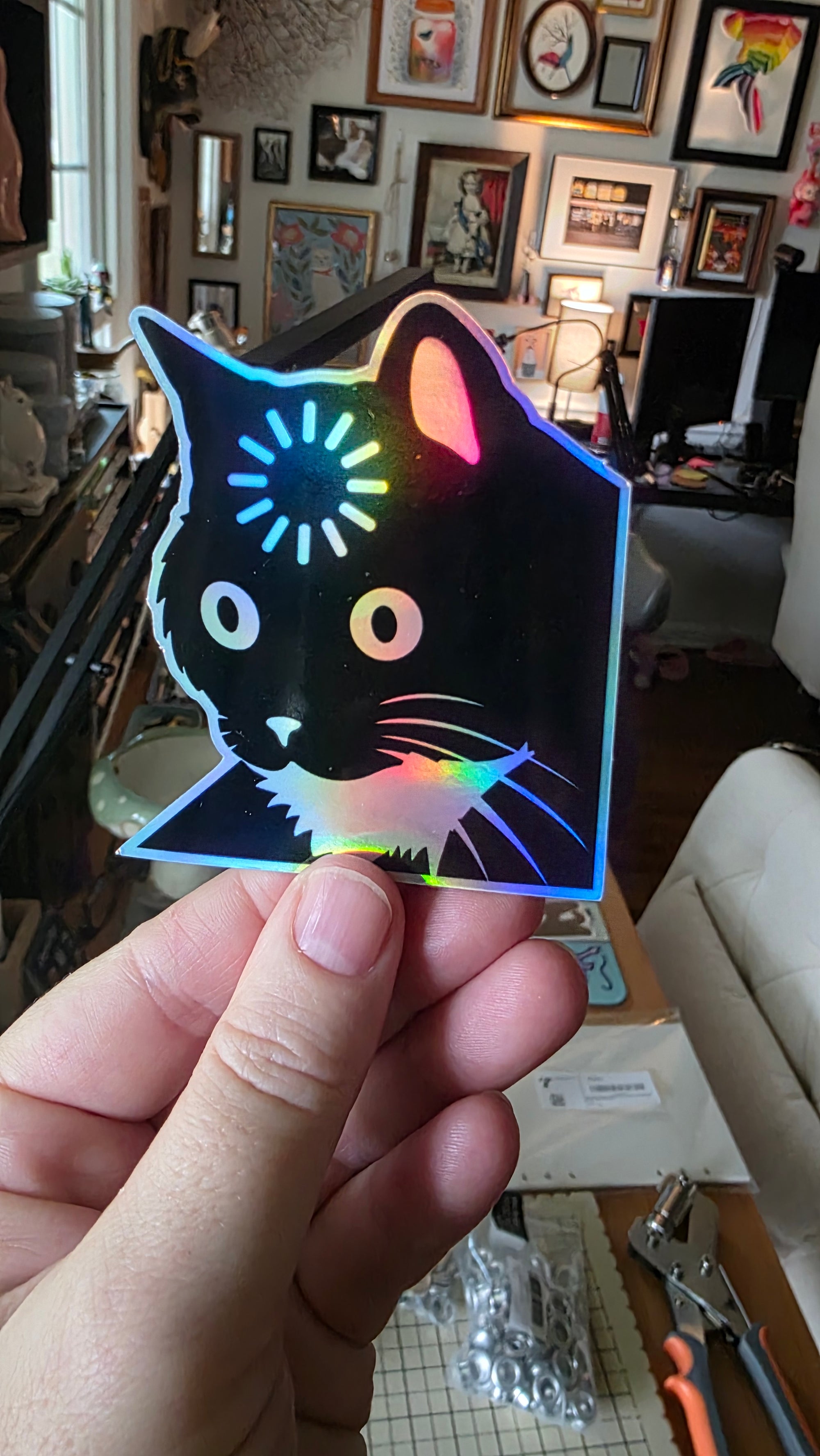 Holographic cat sticker held in a hand with a cluttered room background