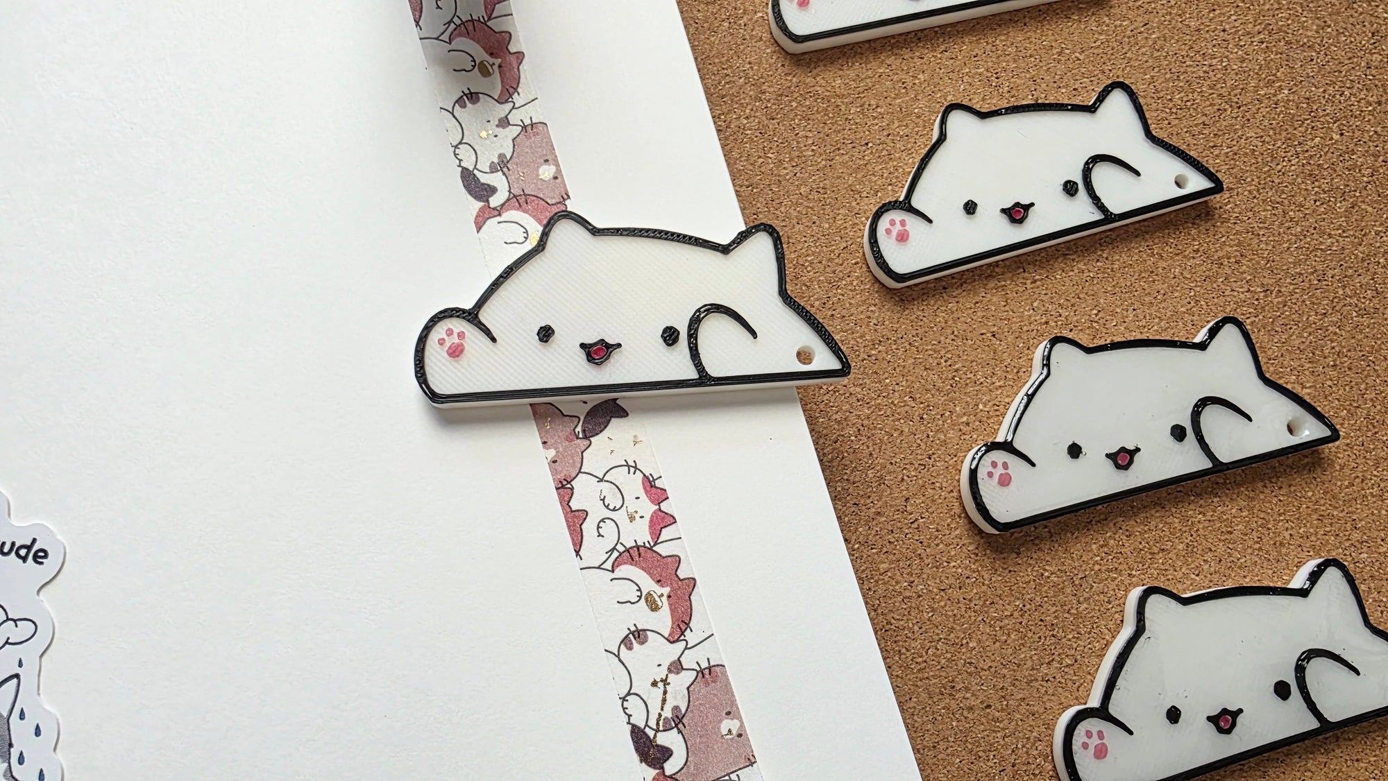 White cat-shaped 3D printed washi tape cutter with black outline, small pink paw detail, smiling face, and a hole on one end.