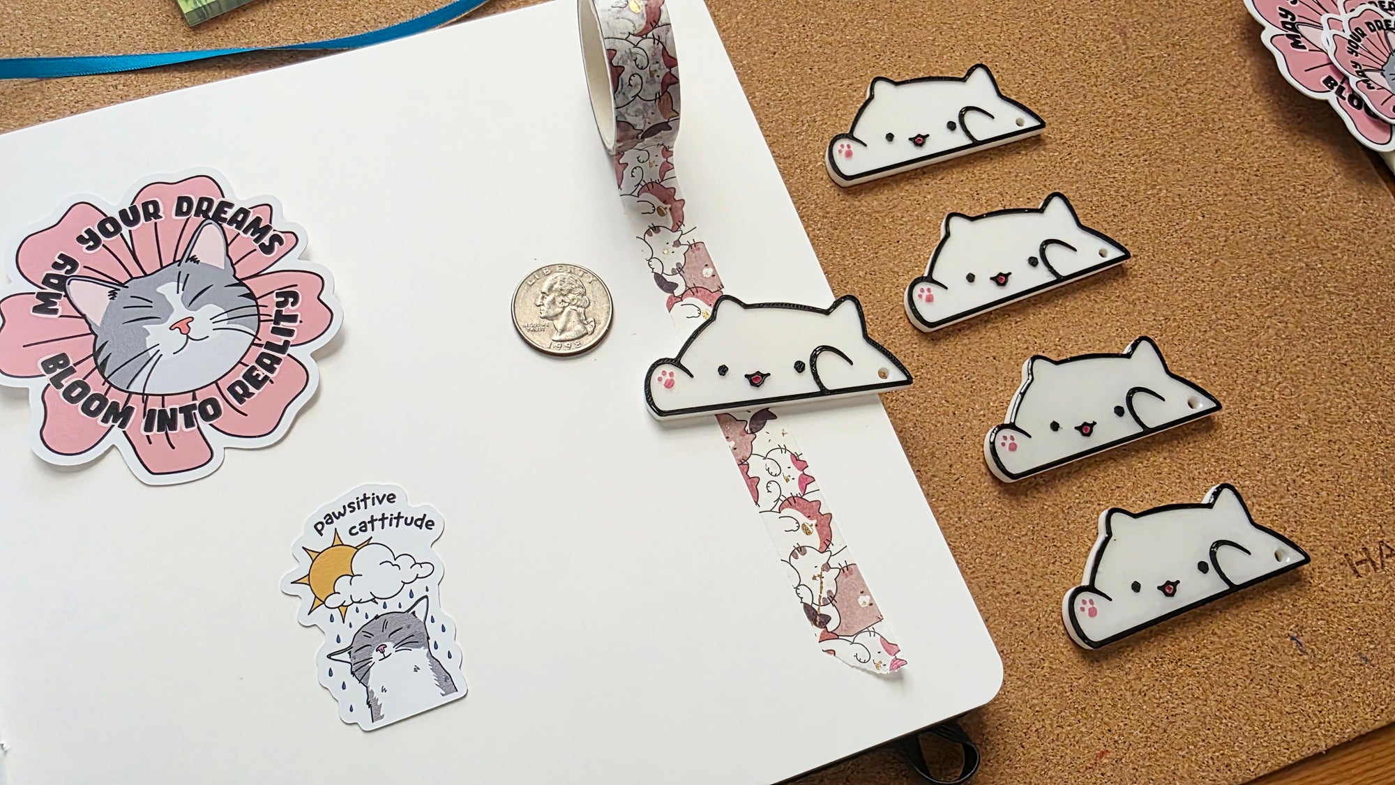 White cat-shaped 3D printed washi tape cutter with black outline, small pink paw detail, smiling face, and a hole on one end.