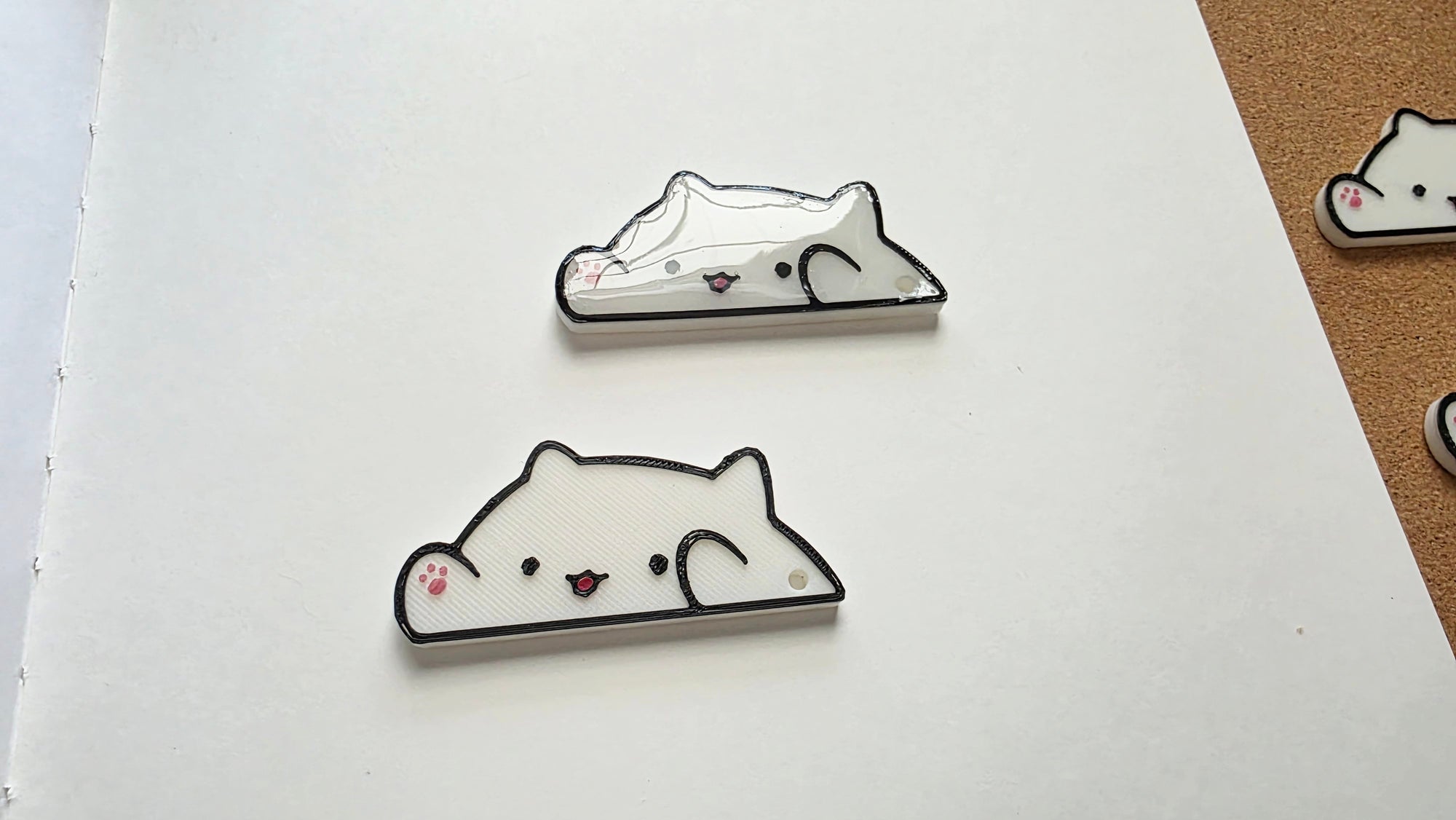 White cat-shaped 3D printed washi tape cutter with black outline, small pink paw detail, smiling face, and a hole on one end.