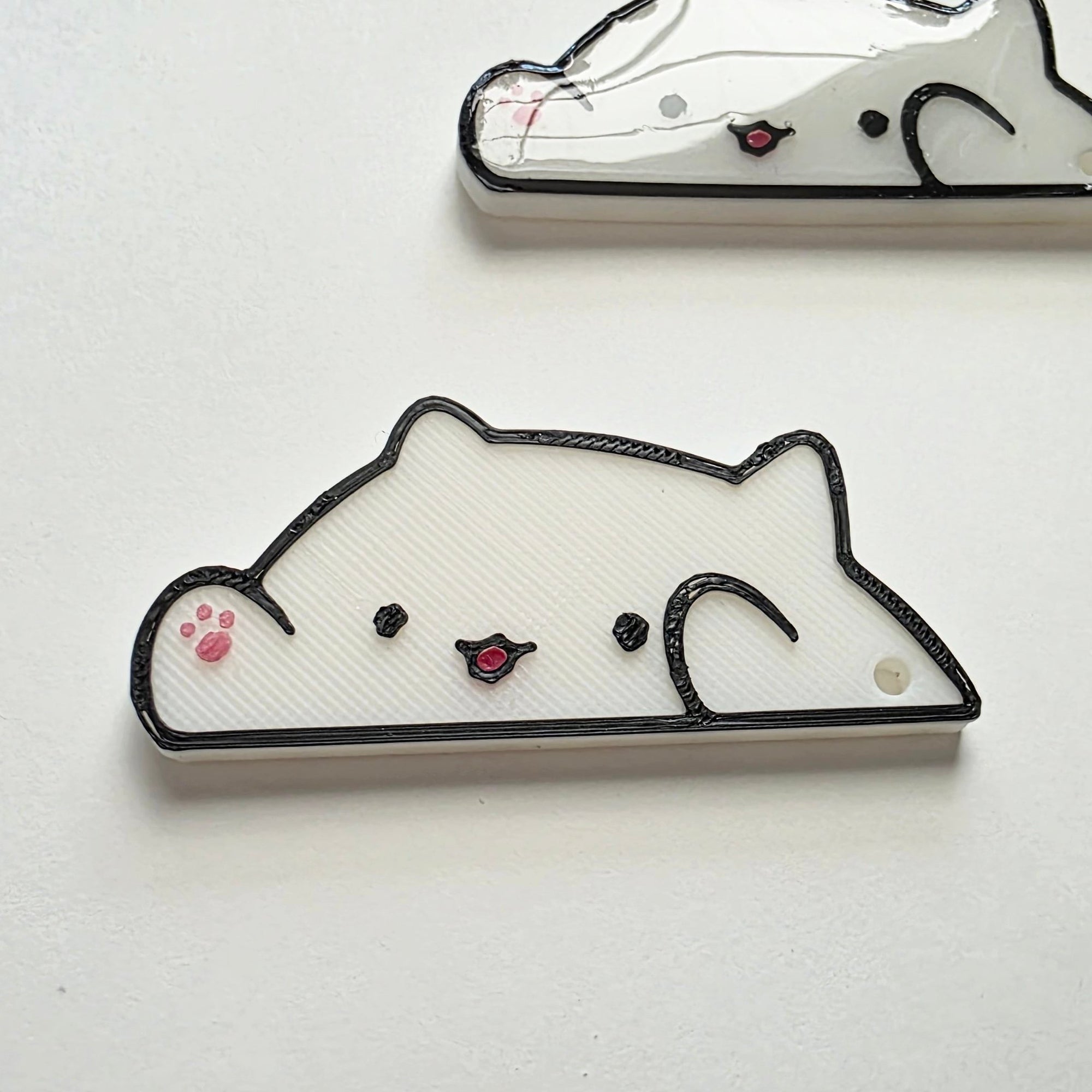 White cat-shaped 3D printed washi tape cutter with black outline, small pink paw detail, smiling face, and a hole on one end.