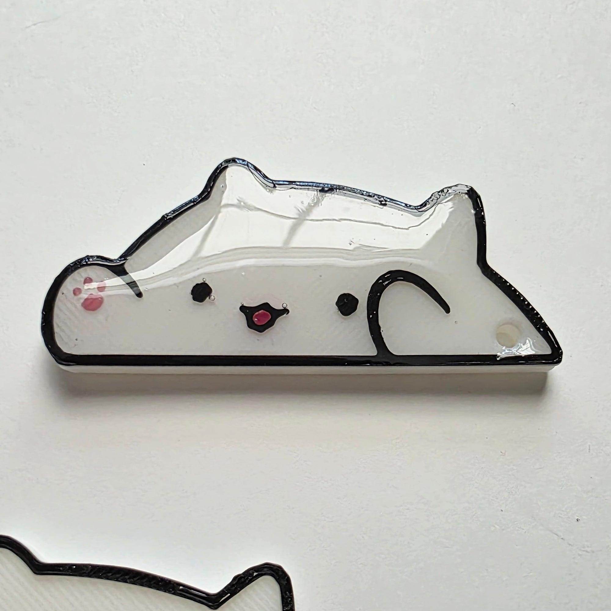White cat-shaped 3D printed washi tape cutter with black outline, small pink paw detail, smiling face, and a hole on one end.