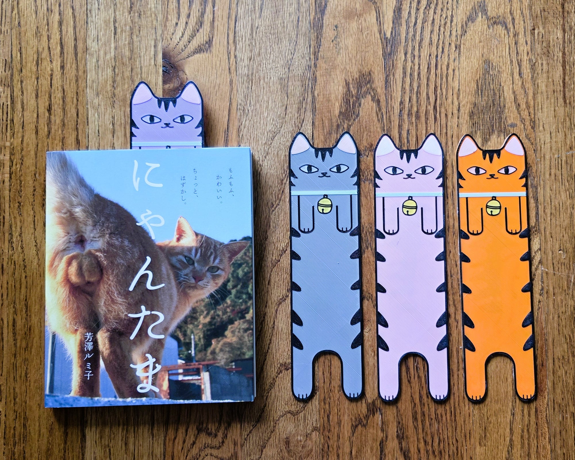 Cat-themed bookmarks on a wooden surface with a book titled 'ニャンたま'.
