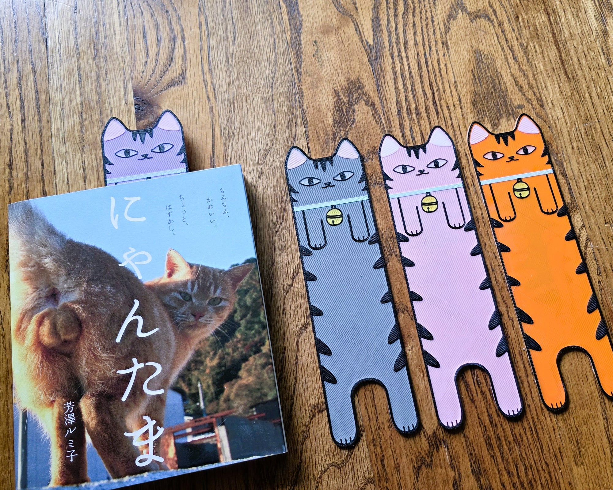 Cat-shaped bookmarks on a wooden surface with a book titled 'ニャンネズミ' in the background.