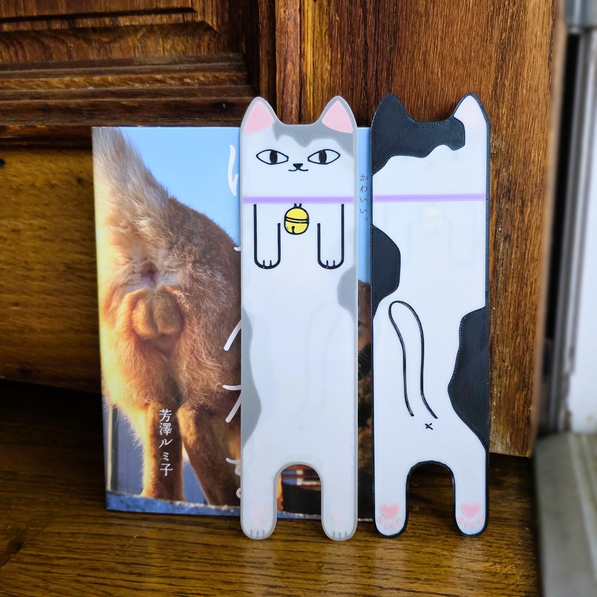 Two cat-shaped phone stands on a wooden surface with a book in the background.