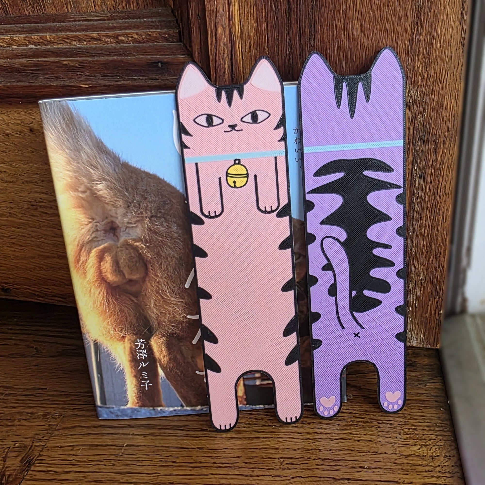 Two cat-shaped bookmarks on a wooden surface