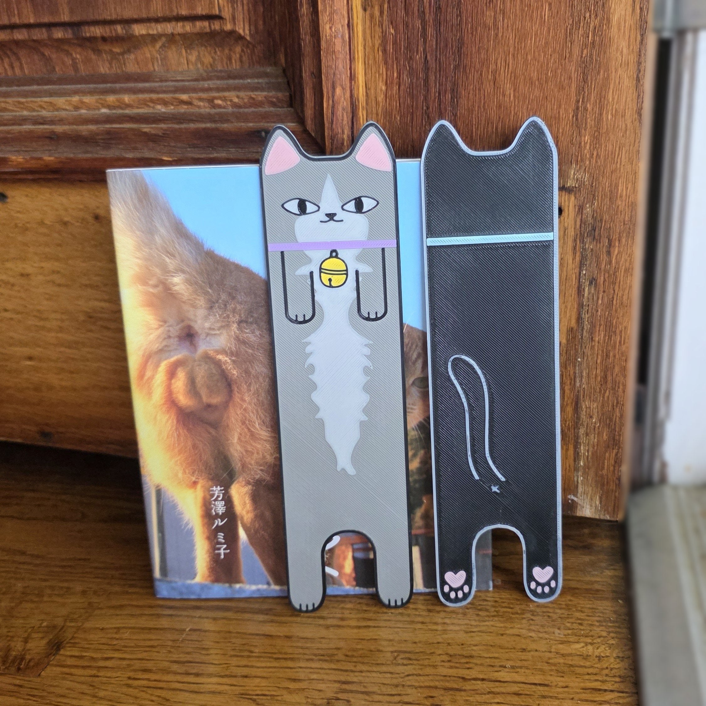 Two cat-shaped bookmarks on a wooden surface