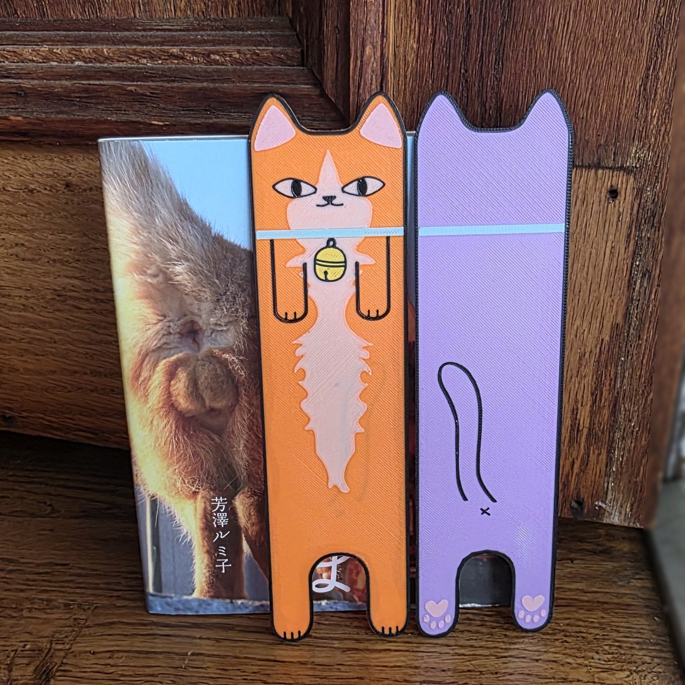Two cat-shaped phone cases, one orange and one purple, on a wooden surface.