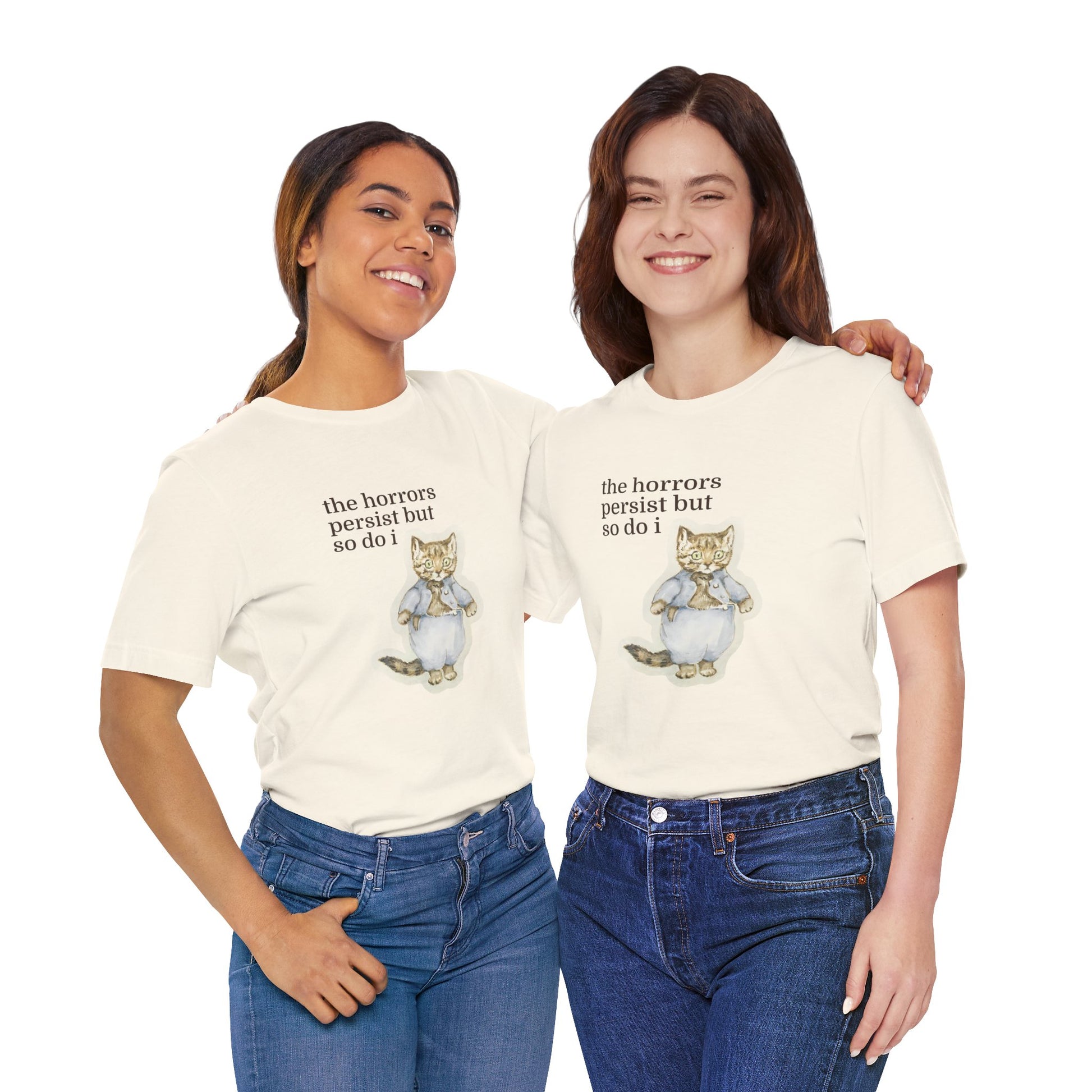 Two women wearing white t-shirt featuring a vintage-style illustrated cat in blue clothing with the phrase “the horrors persist but so do i.”