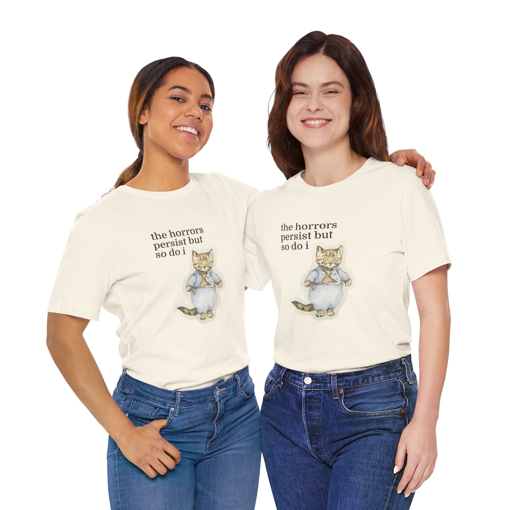 Two women wearing white t-shirt featuring a vintage-style illustrated cat in blue clothing with the phrase “the horrors persist but so do i.”