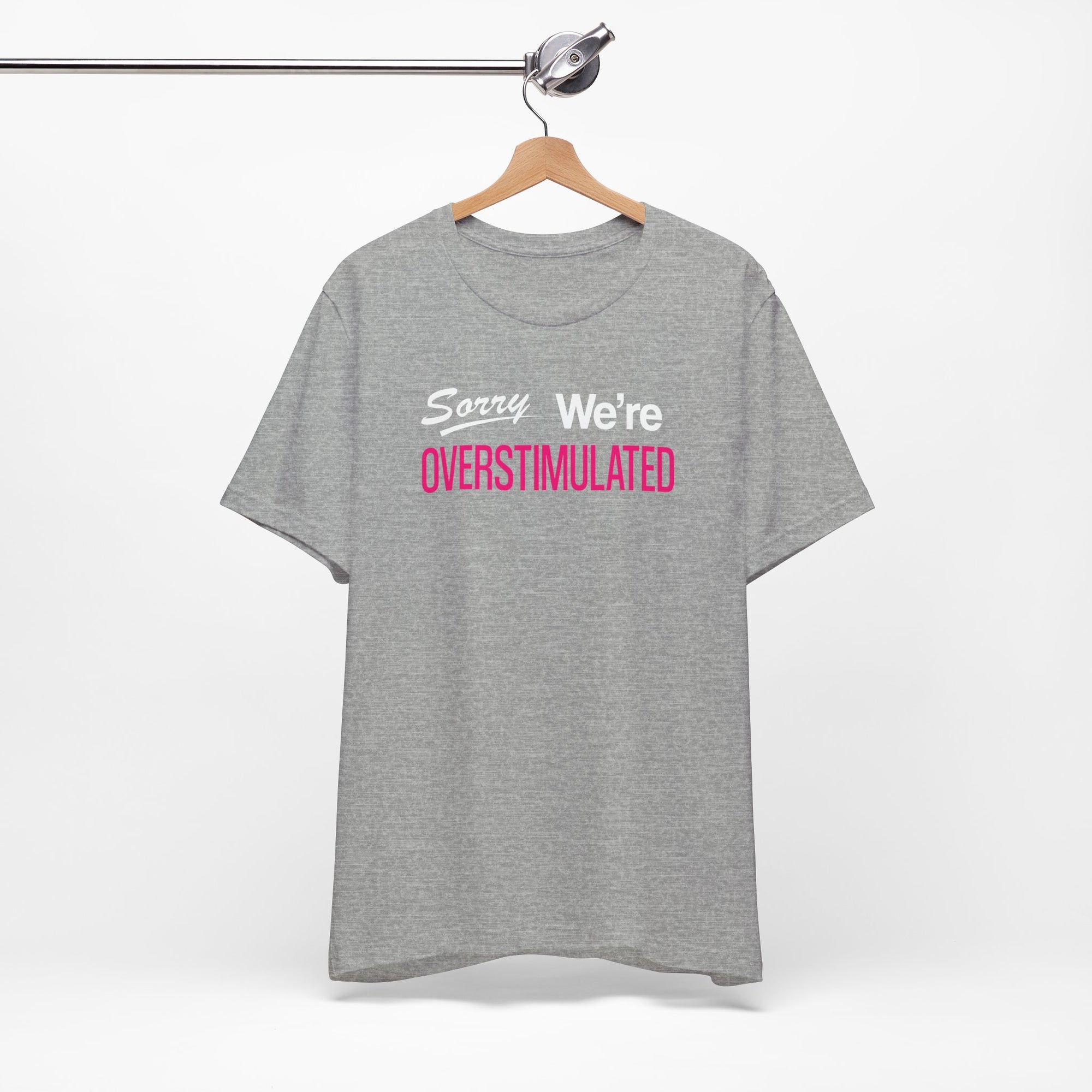 Gray t-shirt featuring the phrase “Sorry We’re Overstimulated” in white and hot pink text.
