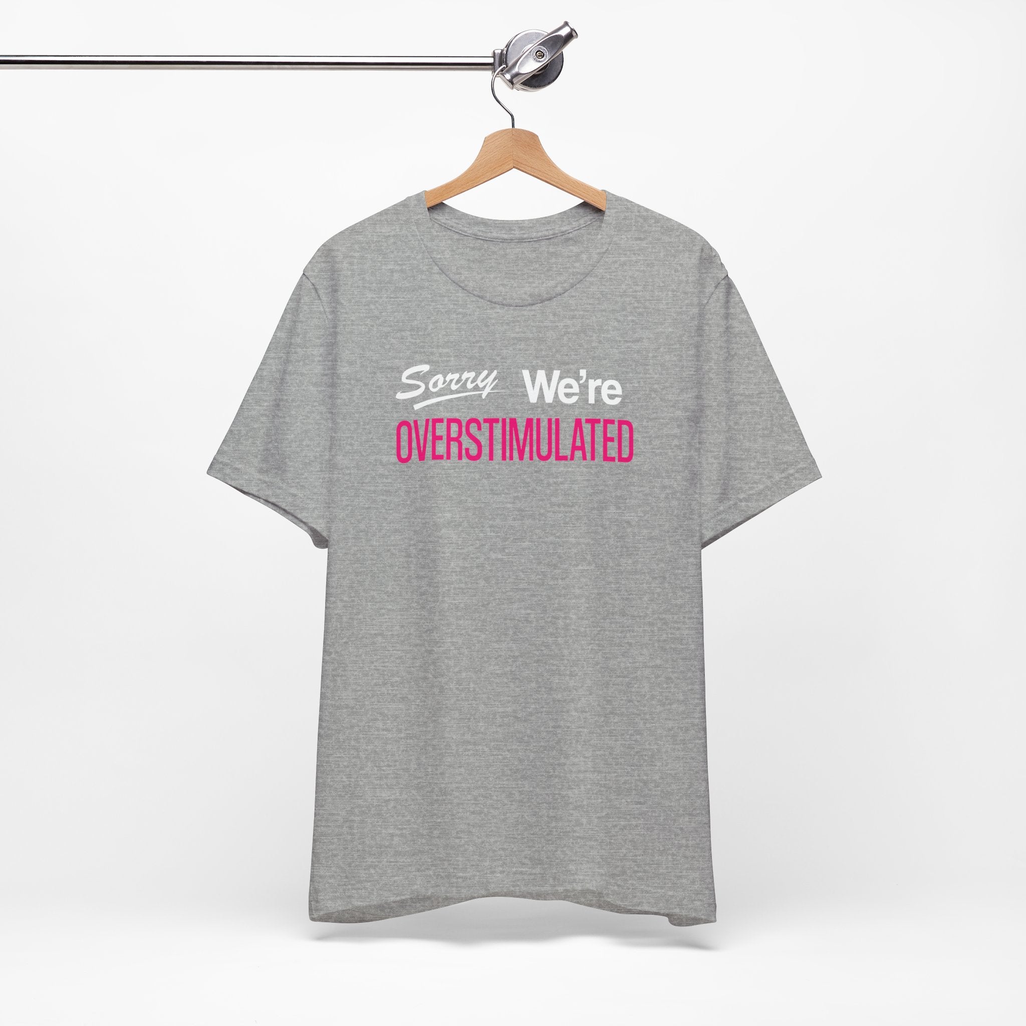Gray t-shirt featuring the phrase “Sorry We’re Overstimulated” in white and hot pink text.
