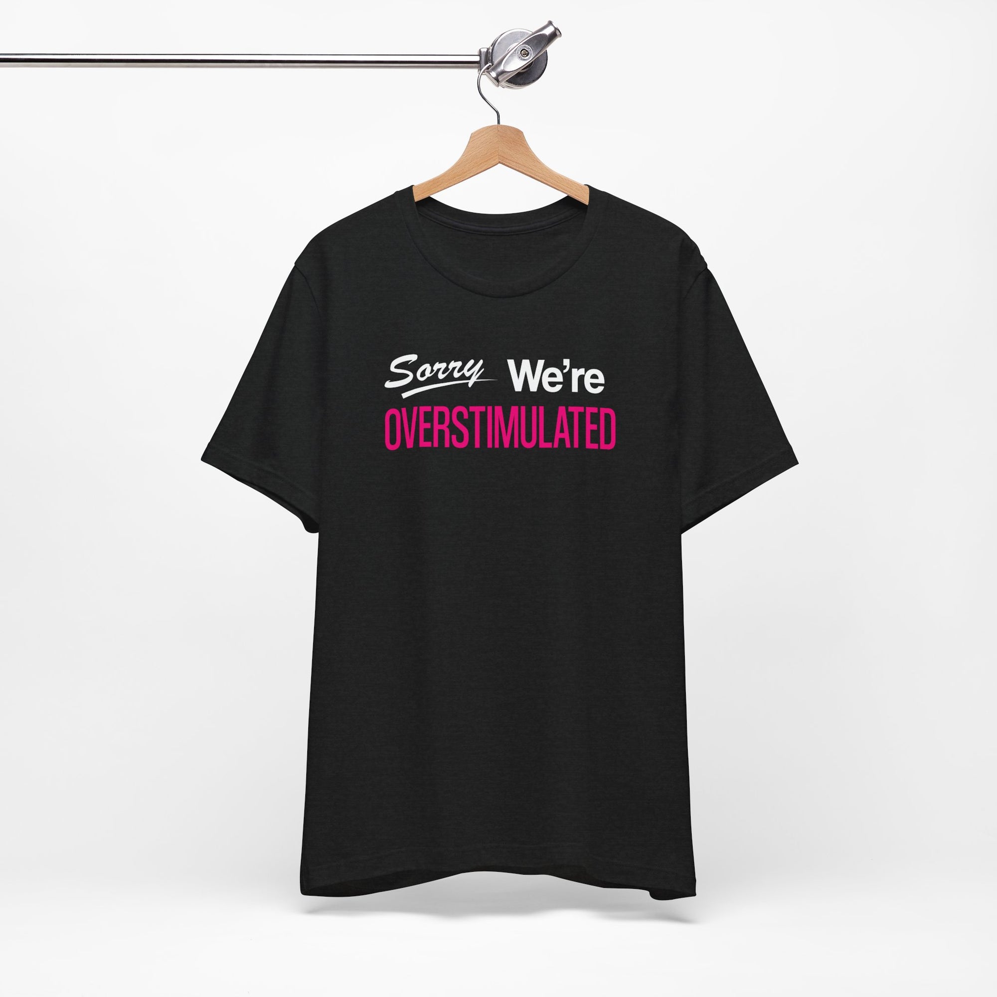 Black t-shirt featuring the phrase “Sorry We’re Overstimulated” in white and hot pink text.
