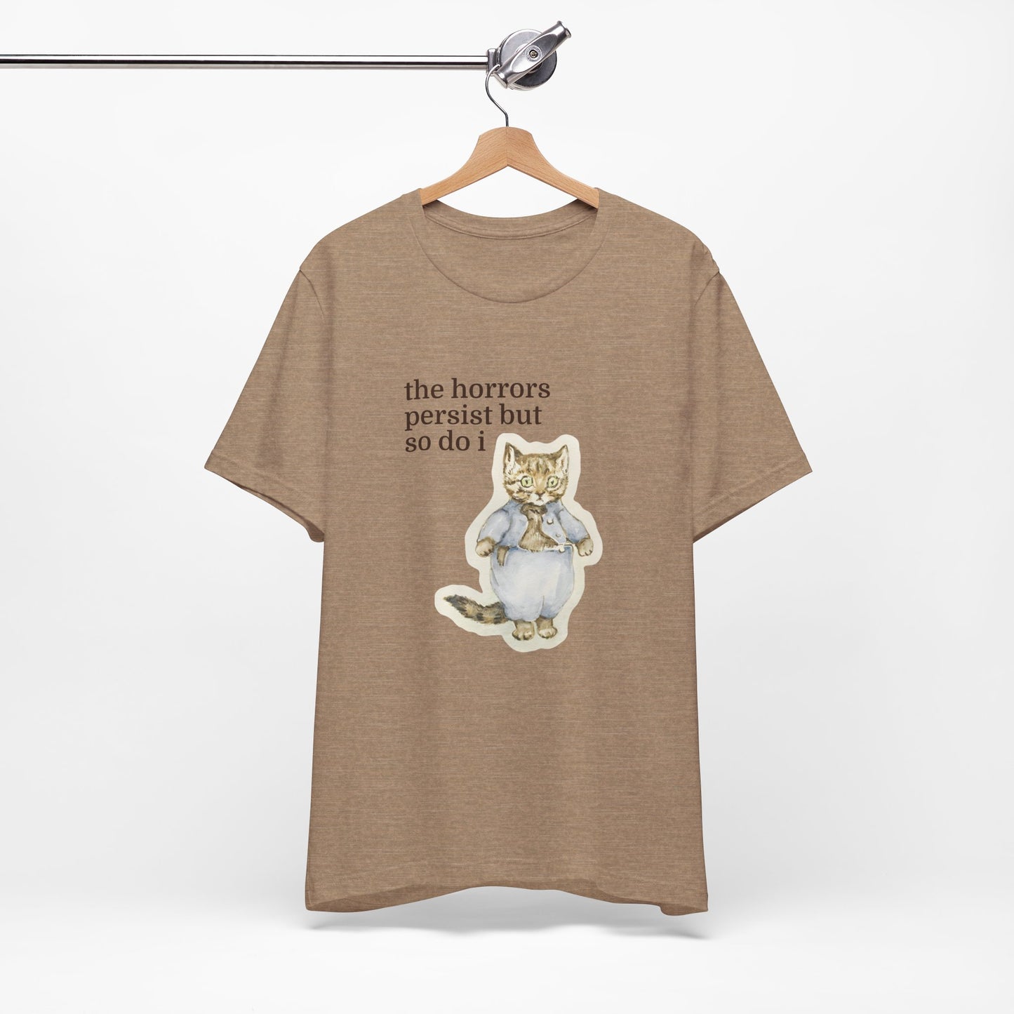 Brown t-shirt featuring a vintage-style illustrated cat in blue clothing with the phrase “the horrors persist but so do i.”