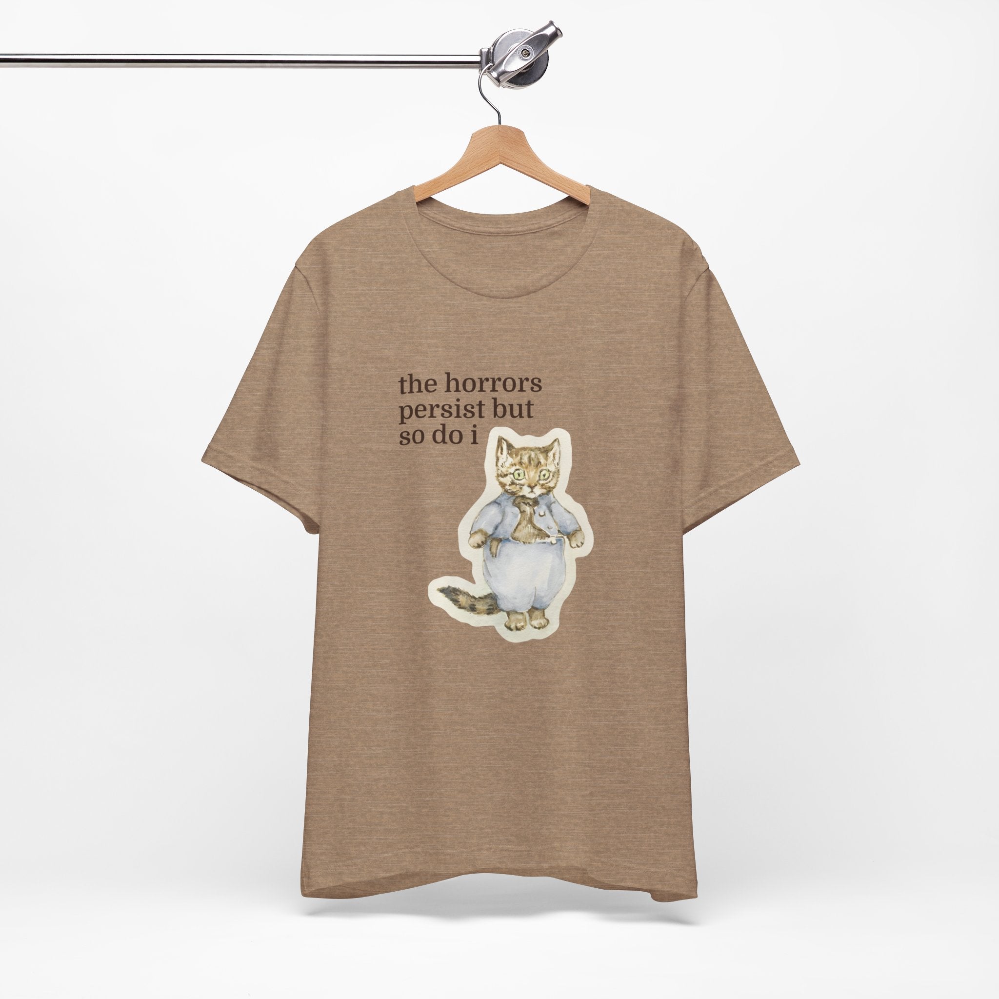 Brown t-shirt featuring a vintage-style illustrated cat in blue clothing with the phrase “the horrors persist but so do i.”