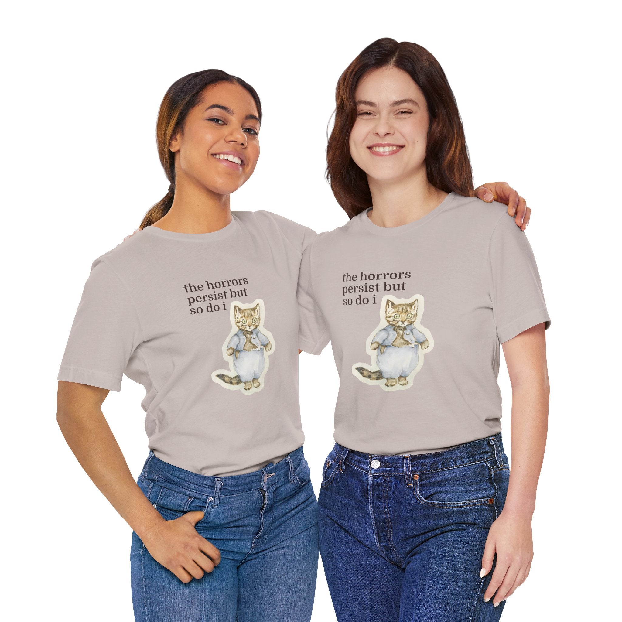 Two people wearing beige t-shirt featuring a vintage-style illustrated cat in blue clothing with the phrase “the horrors persist but so do i.”