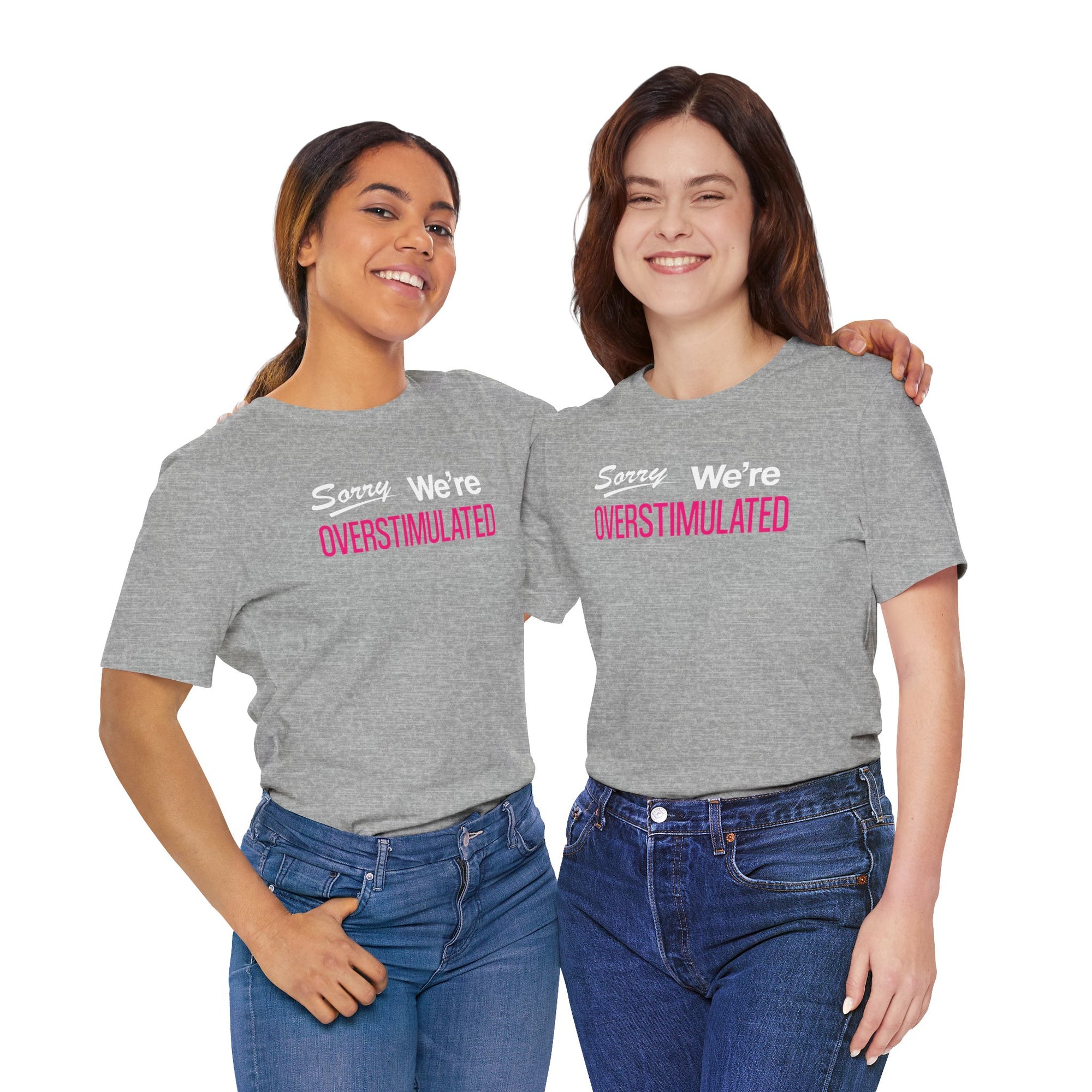 Two people wearing gray t-shirt featuring the phrase “Sorry We’re Overstimulated” in white and hot pink text.
