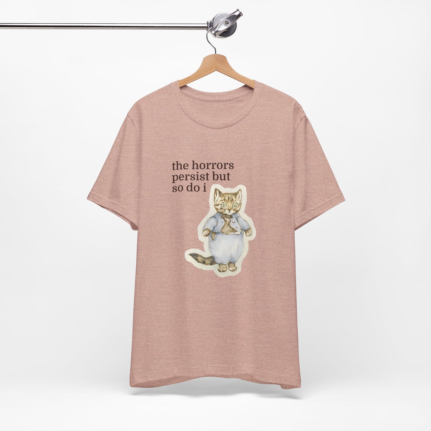 Peach t-shirt featuring a vintage-style illustrated cat in blue clothing with the phrase “the horrors persist but so do i.”