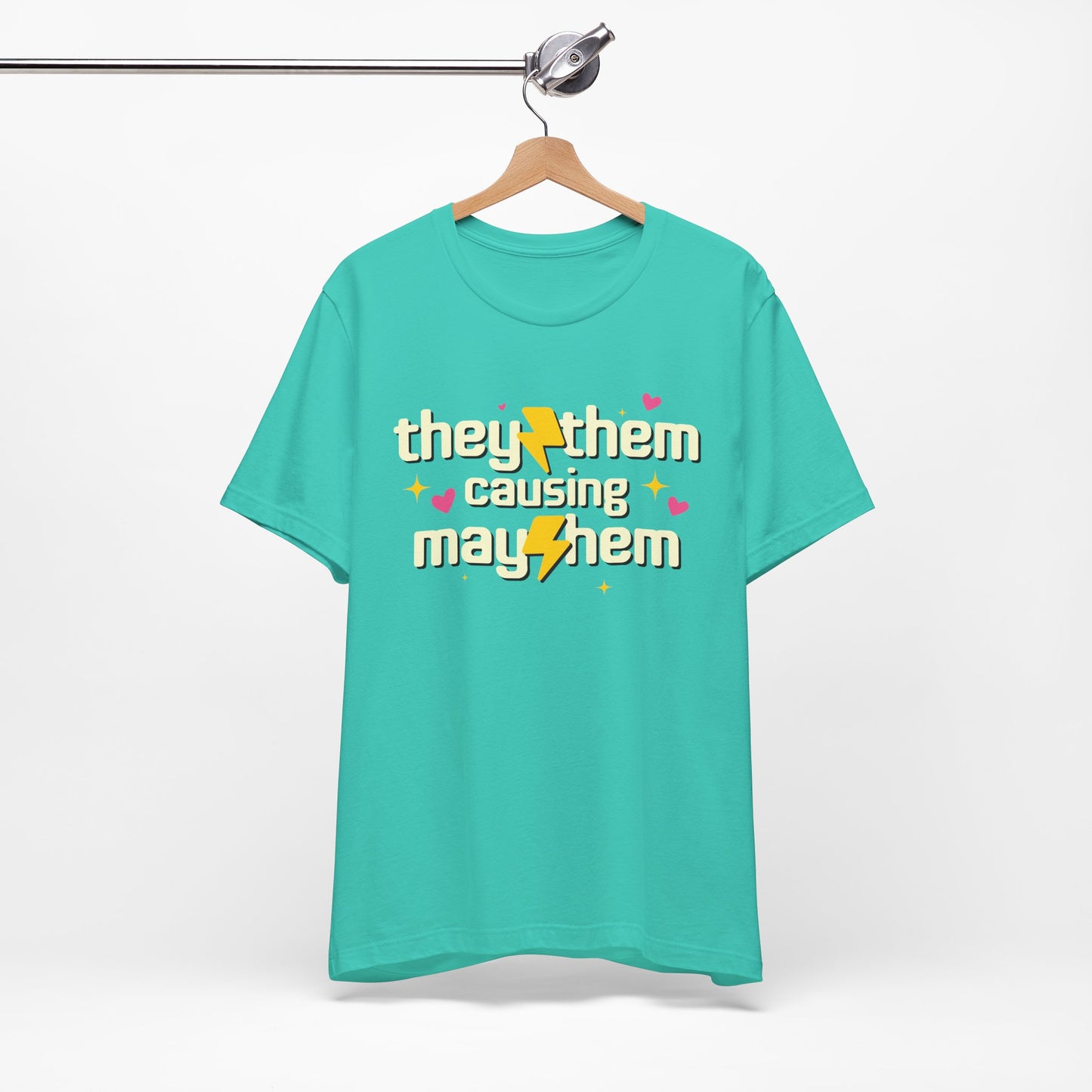 Turquoise t-shirt with 'they/them causing mayhem' text on a hanger against a white background