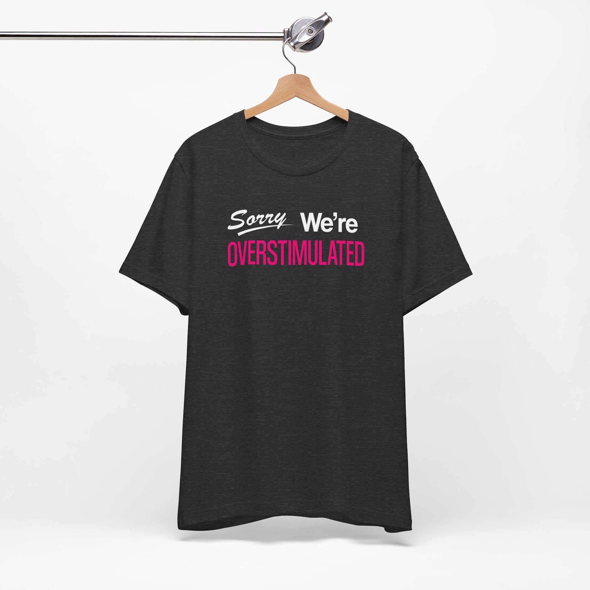 black t-shirt featuring the phrase “Sorry We’re Overstimulated” in white and hot pink text.
