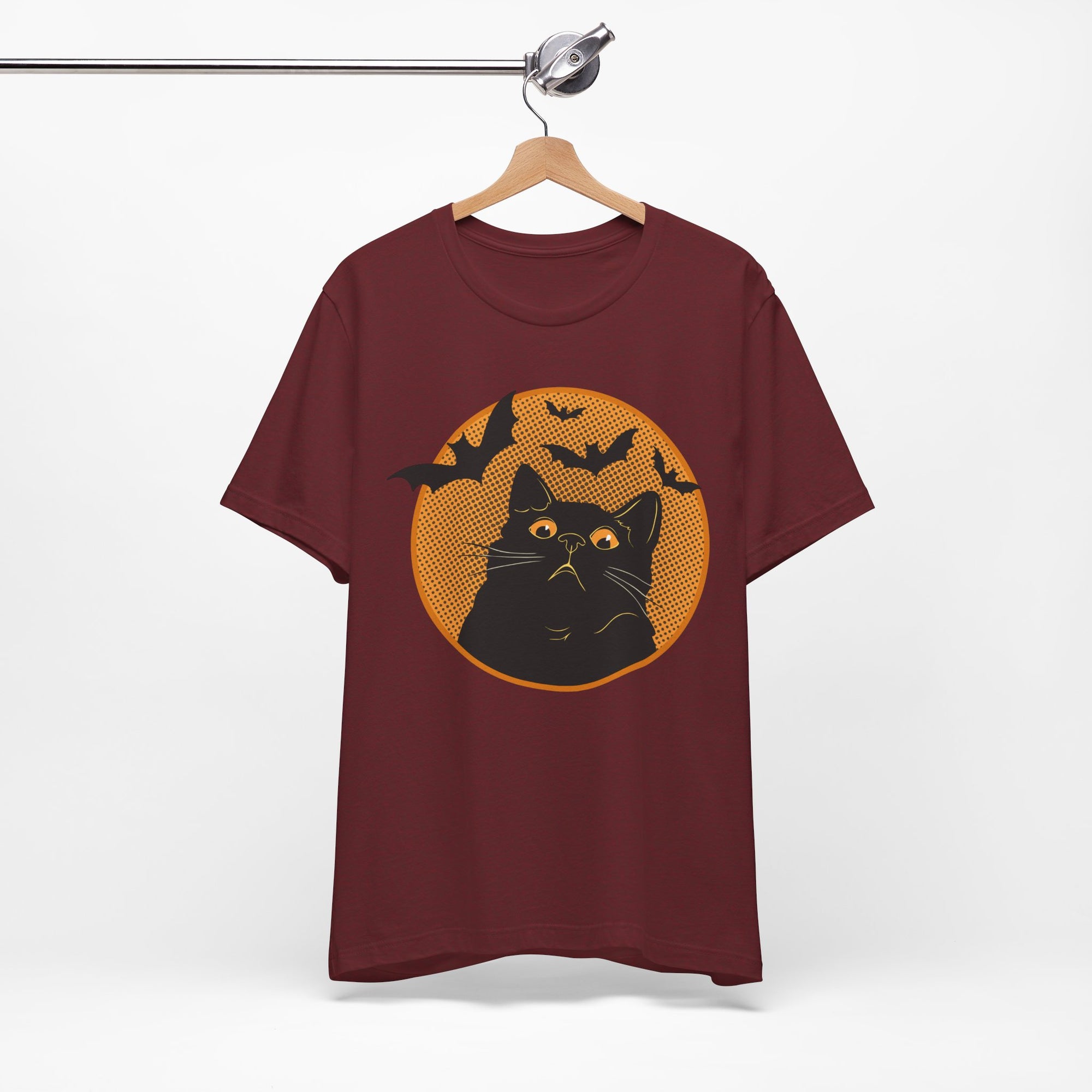 Maroon t-shirt featuring a retro-style black cat graphic with orange moon, flying bats, and Halloween-inspired details.