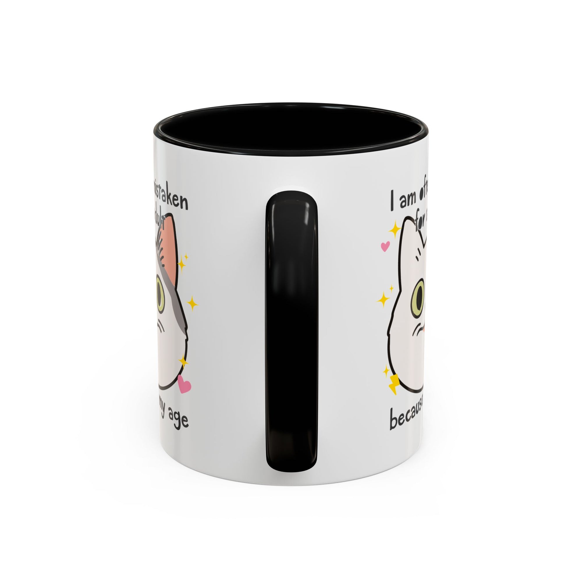 White ceramic mug with black handle and interior featuring a cute wide-eyed cat face, hearts, sparkles, and the phrase “I am often mistaken for an adult because of my age.”
