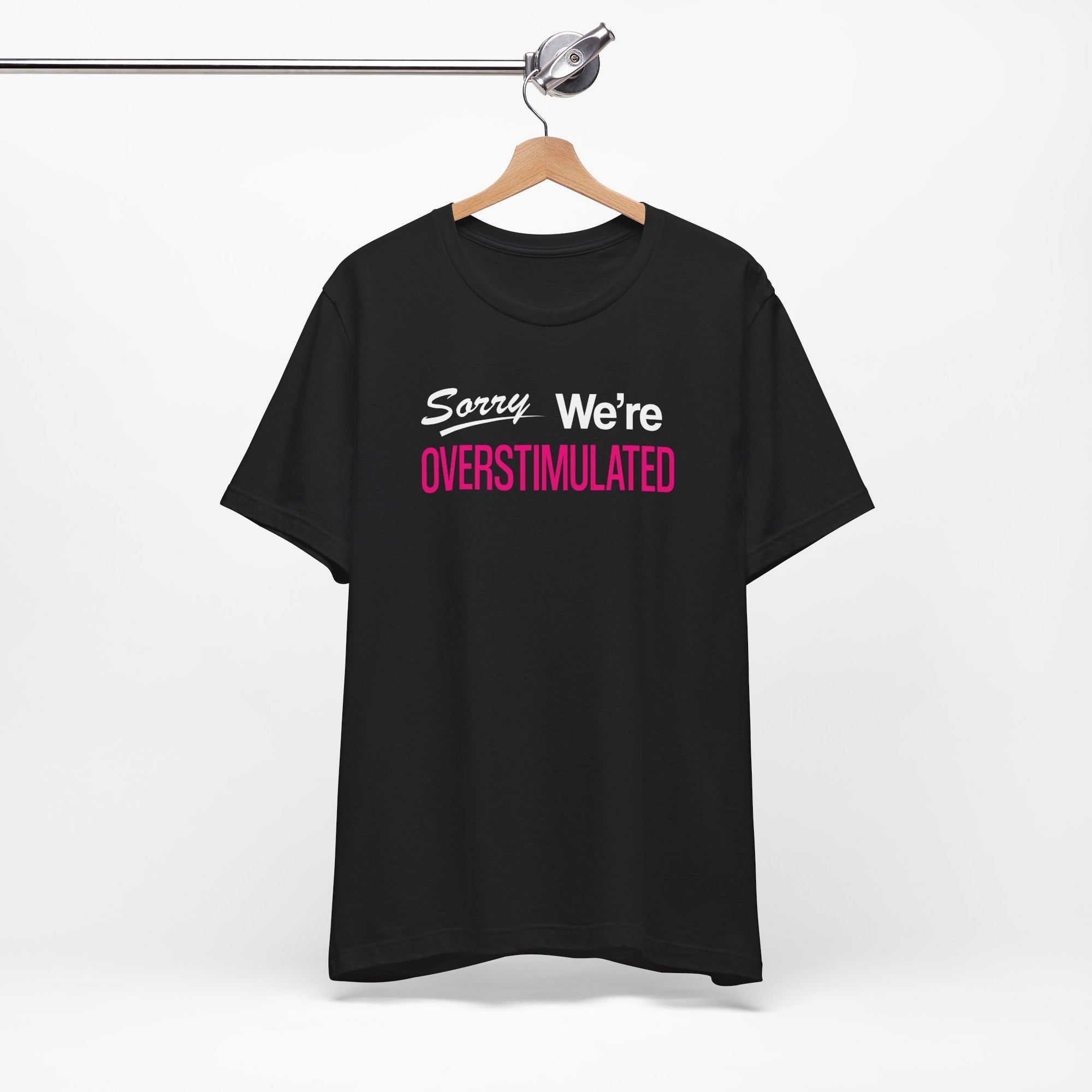Black t-shirt featuring the phrase “Sorry We’re Overstimulated” in white and hot pink text.
