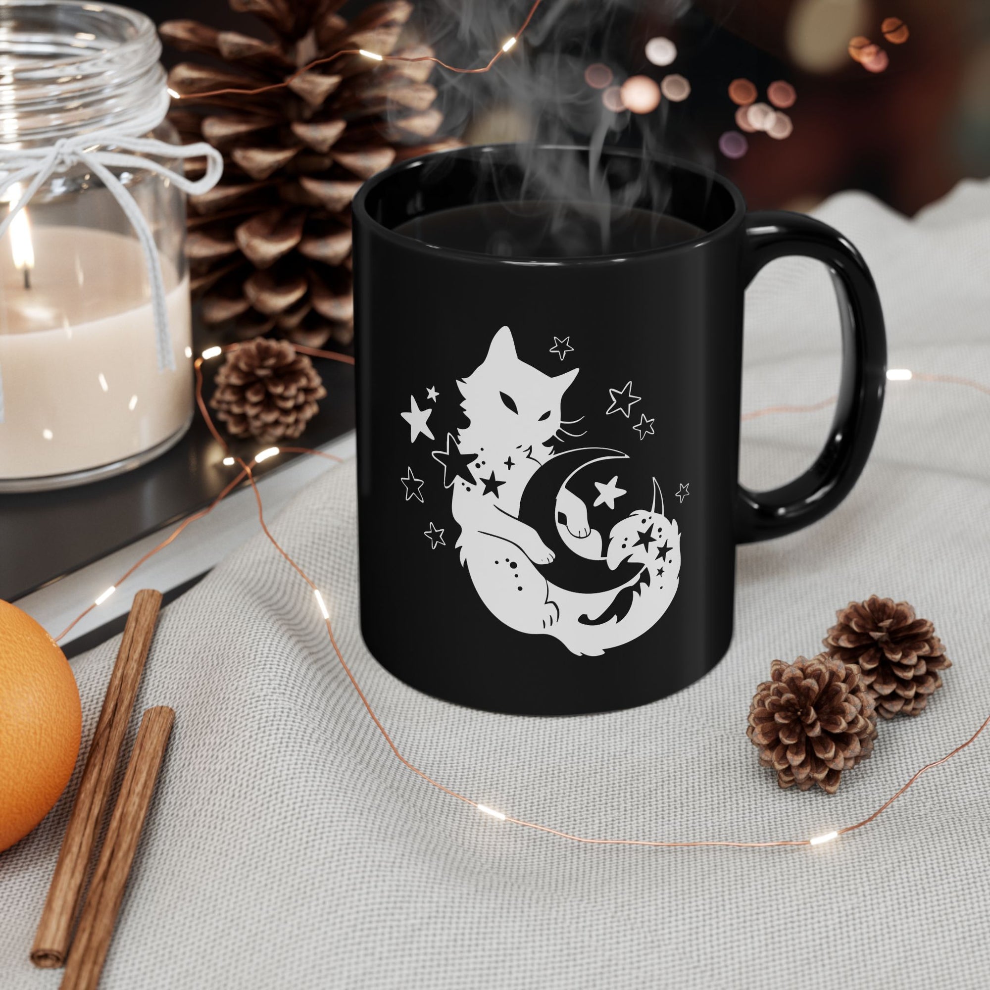 Black mug with a cat and moon design, surrounded by decorative items on a table.
