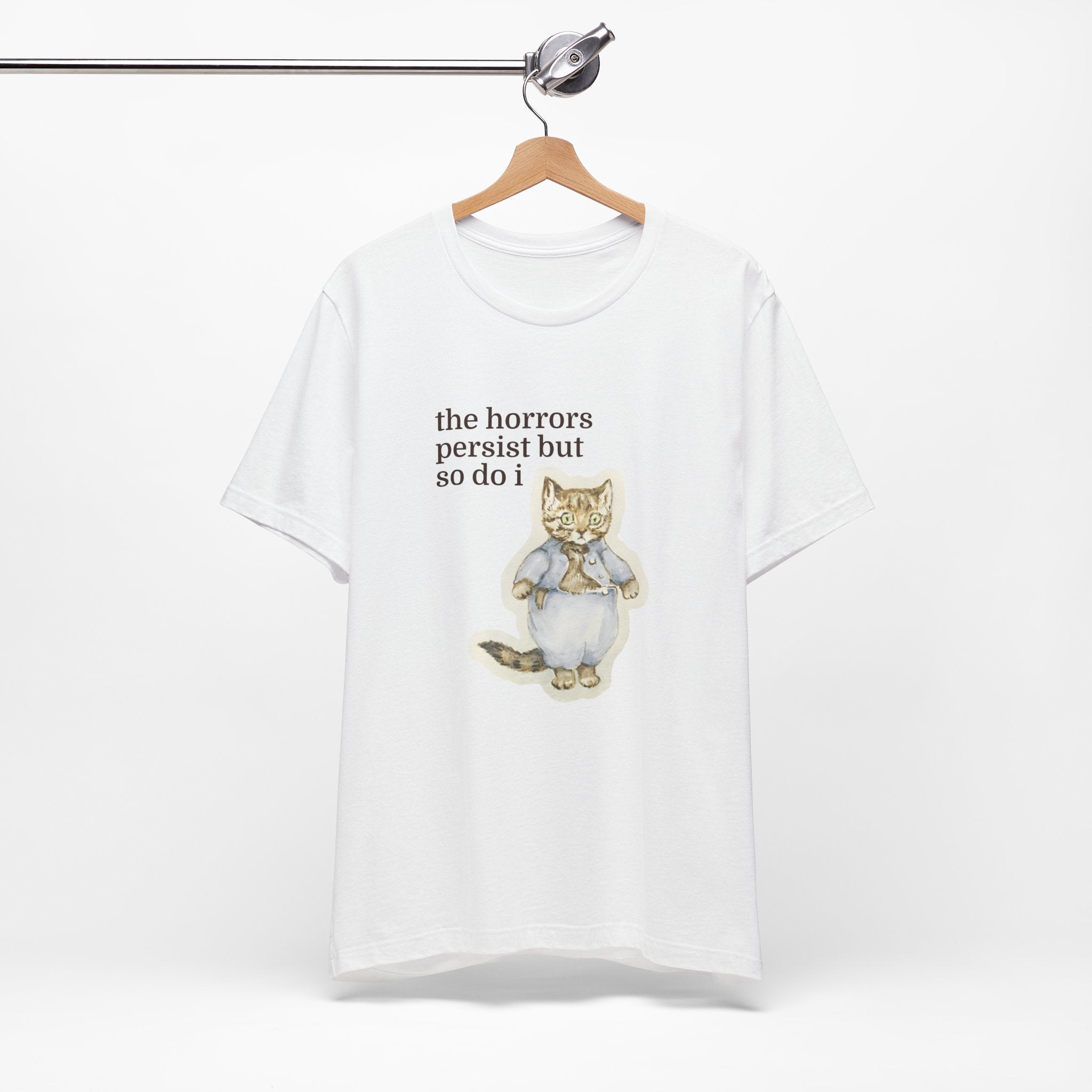 White t-shirt featuring a vintage-style illustrated cat in blue clothing with the phrase “the horrors persist but so do i.”