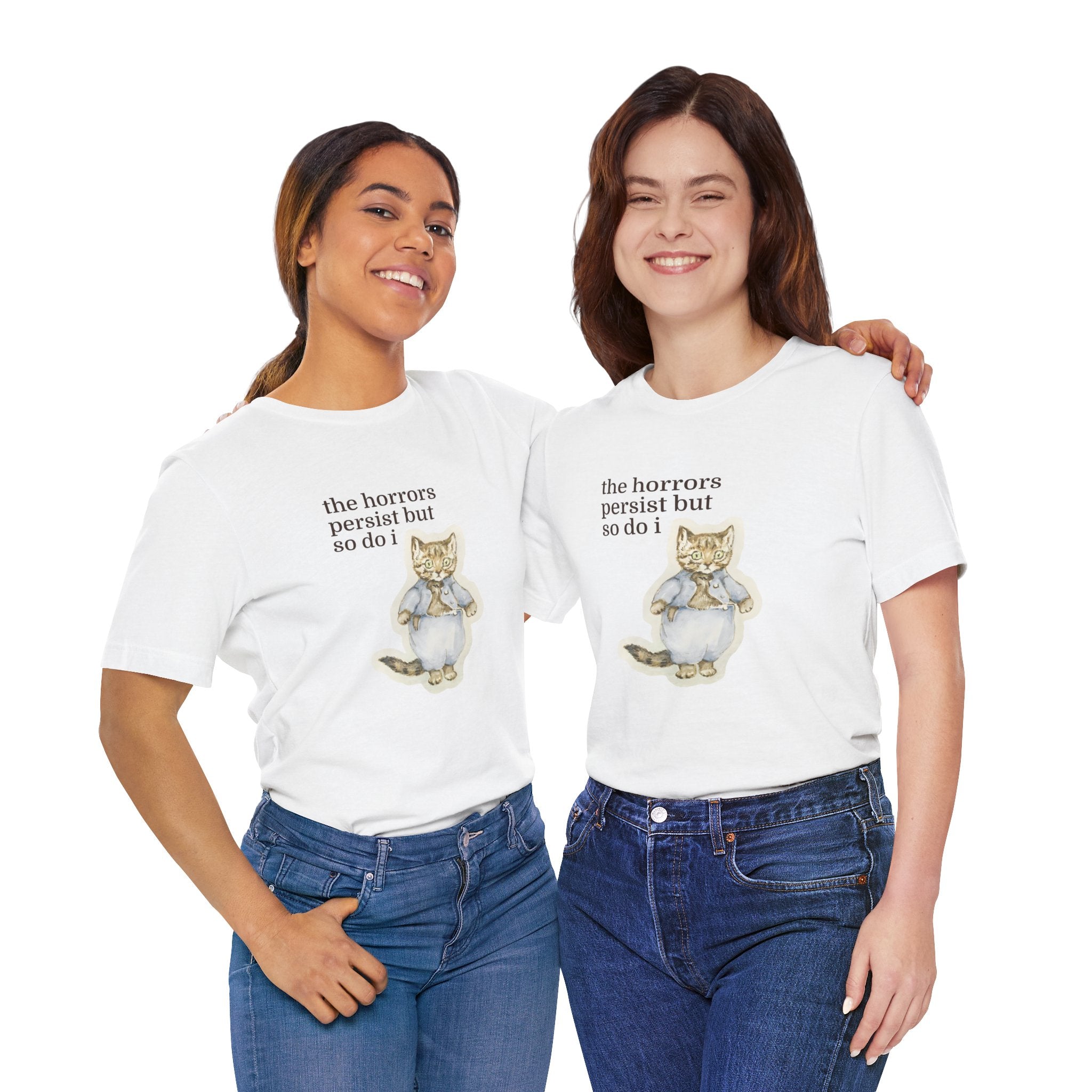 Two women wearing white t-shirt featuring a vintage-style illustrated cat in blue clothing with the phrase “the horrors persist but so do i.”
