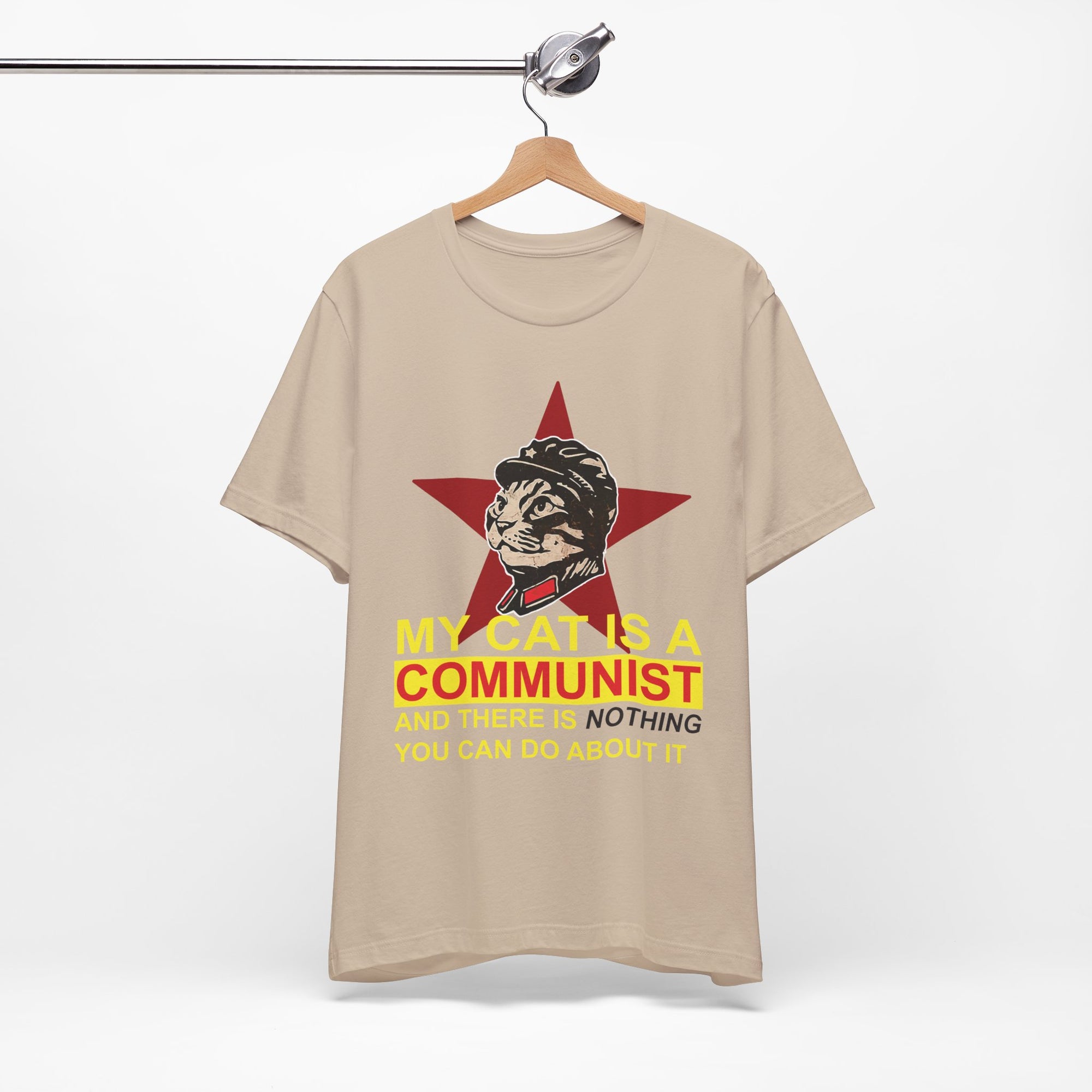 Beige t-shirt with a graphic of a cat in a communist uniform and text on a hanger against a white background