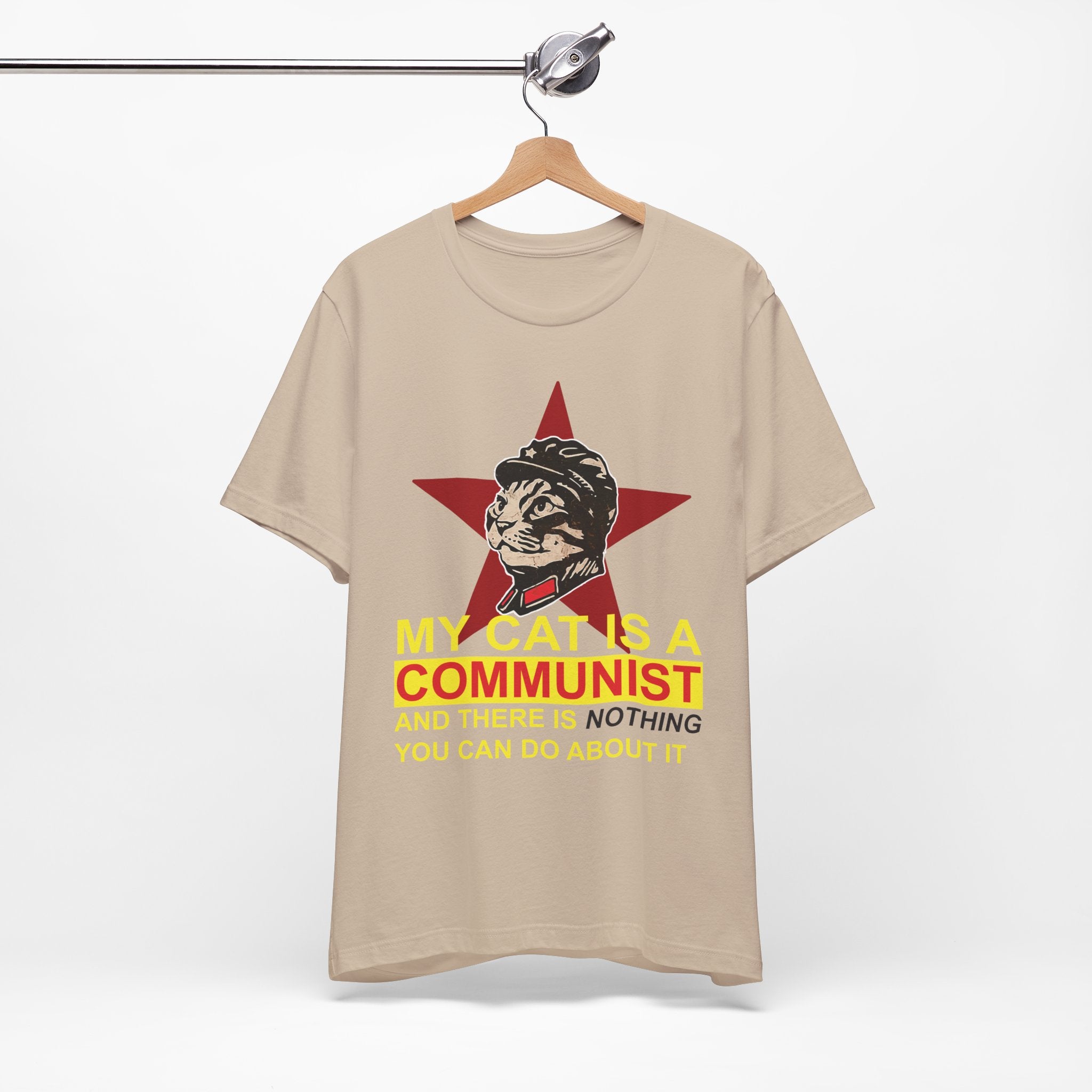 Beige t-shirt with a graphic of a cat in a communist uniform and text on a hanger against a white background