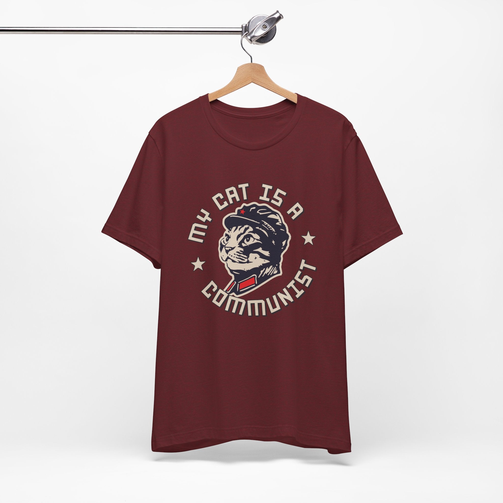 Maroon t-shirt with a graphic design of a cat and text on a hanger against a white background