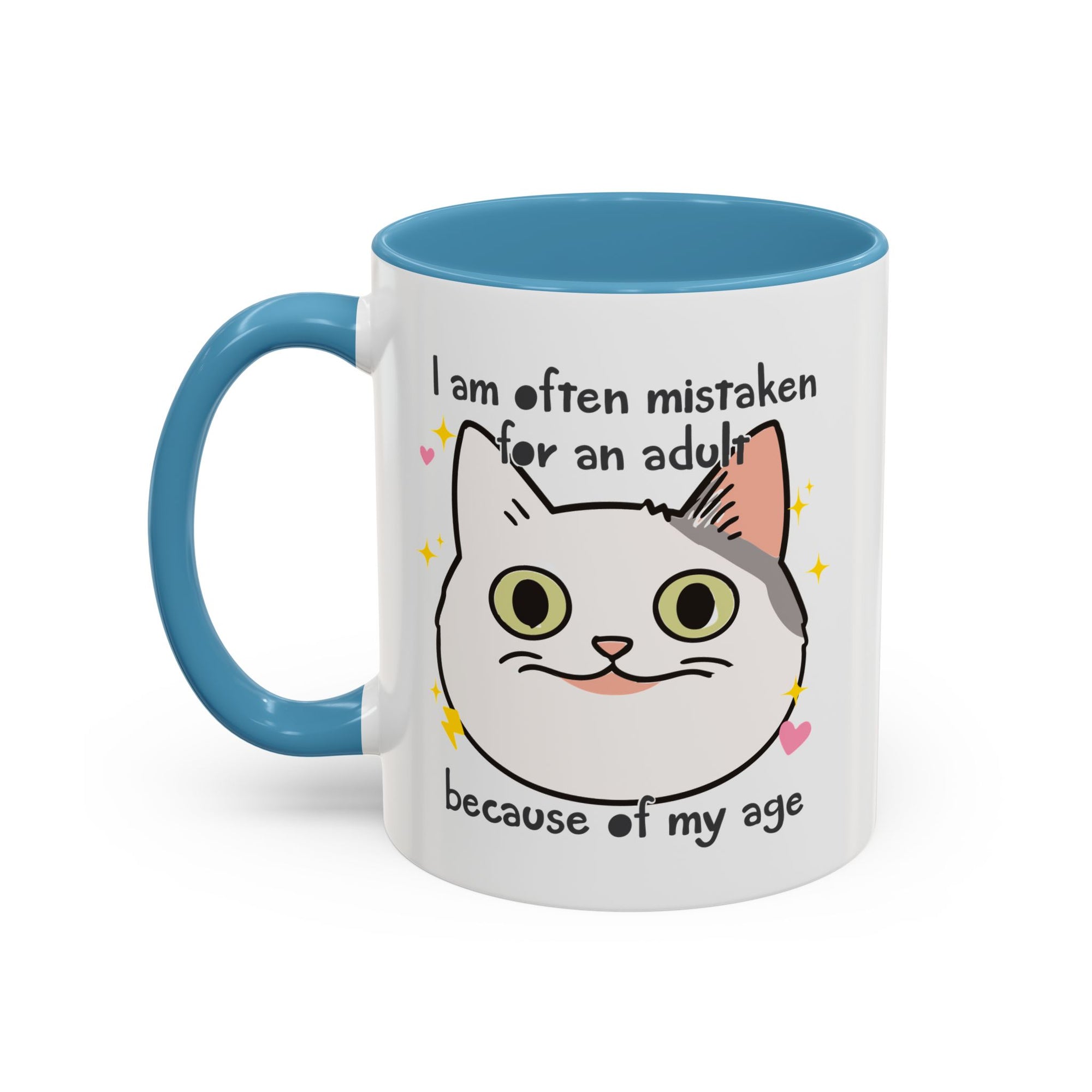 White ceramic mug with blue handle and interior featuring a cute wide-eyed cat face, hearts, sparkles, and the phrase “I am often mistaken for an adult because of my age.”
