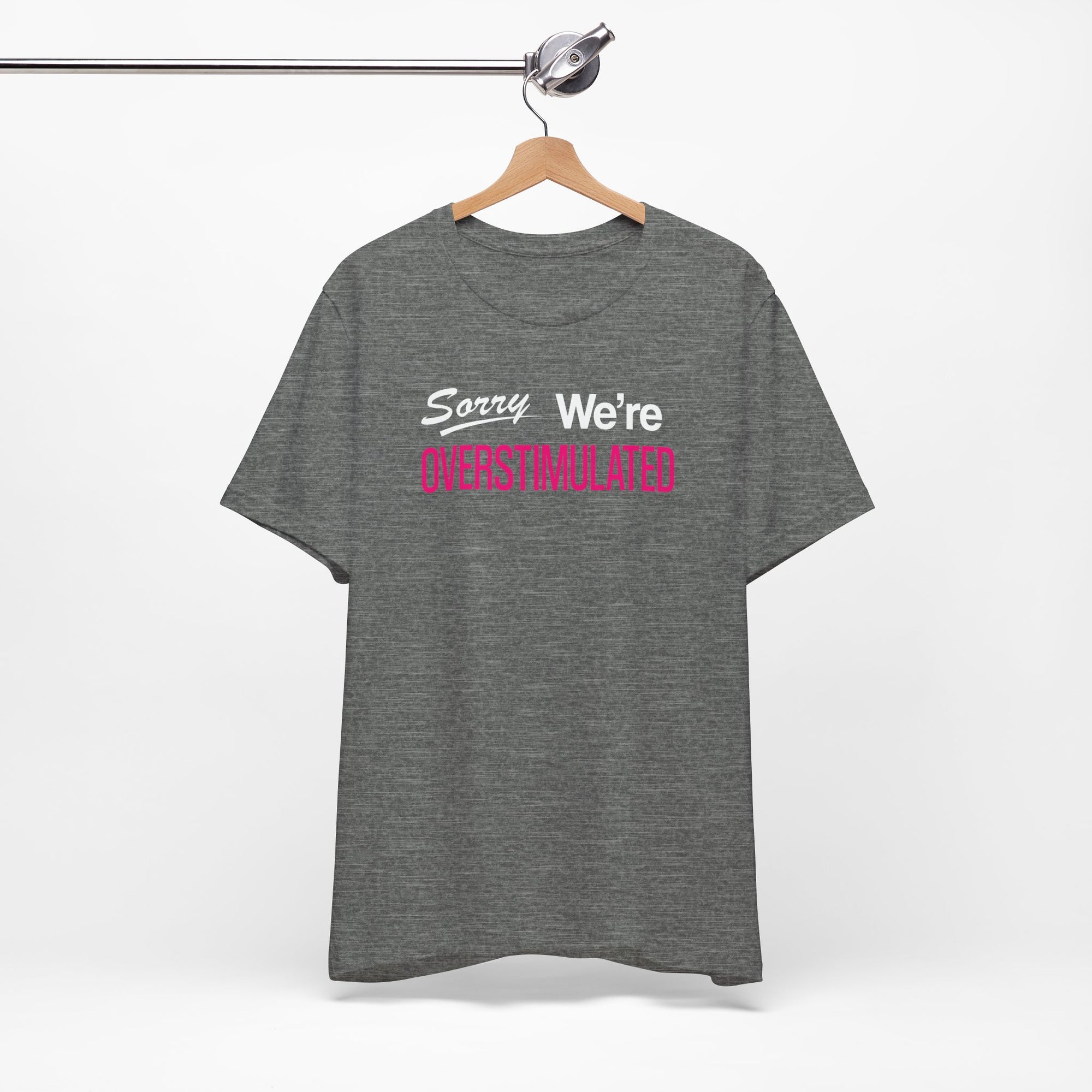 Grey t-shirt featuring the phrase “Sorry We’re Overstimulated” in white and hot pink text.

